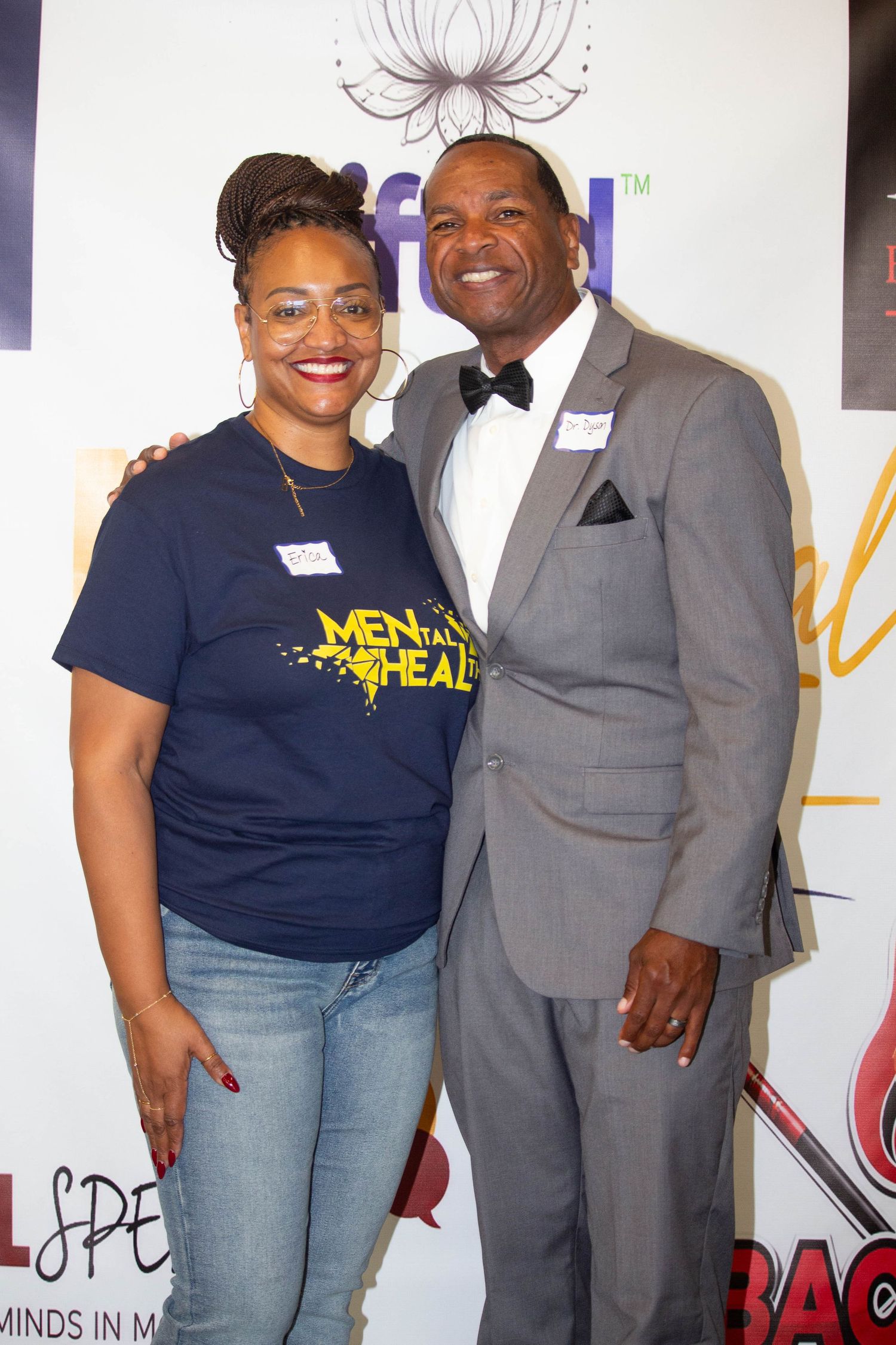 Two people posing together at a mental health awareness event, woman in navy tee and man in gray suit with bow tie.