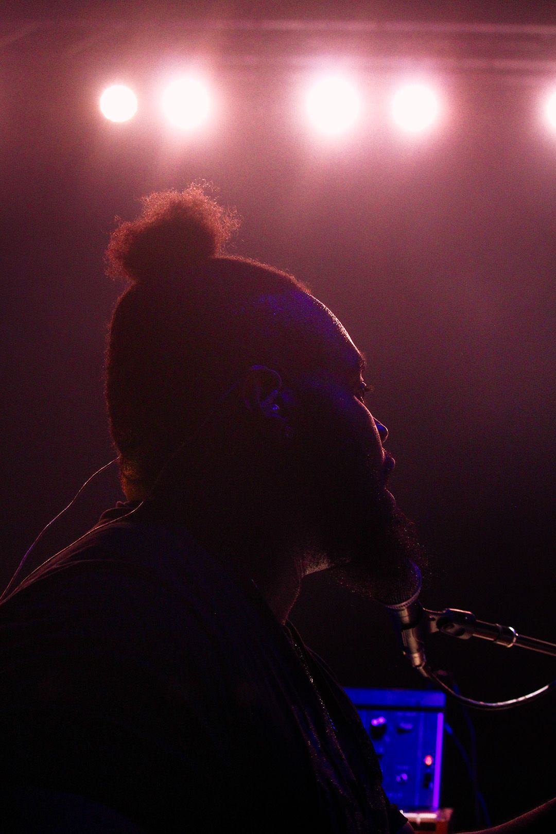 Silhouetted musician performing on stage with dramatic pink and purple stage lighting overhead.