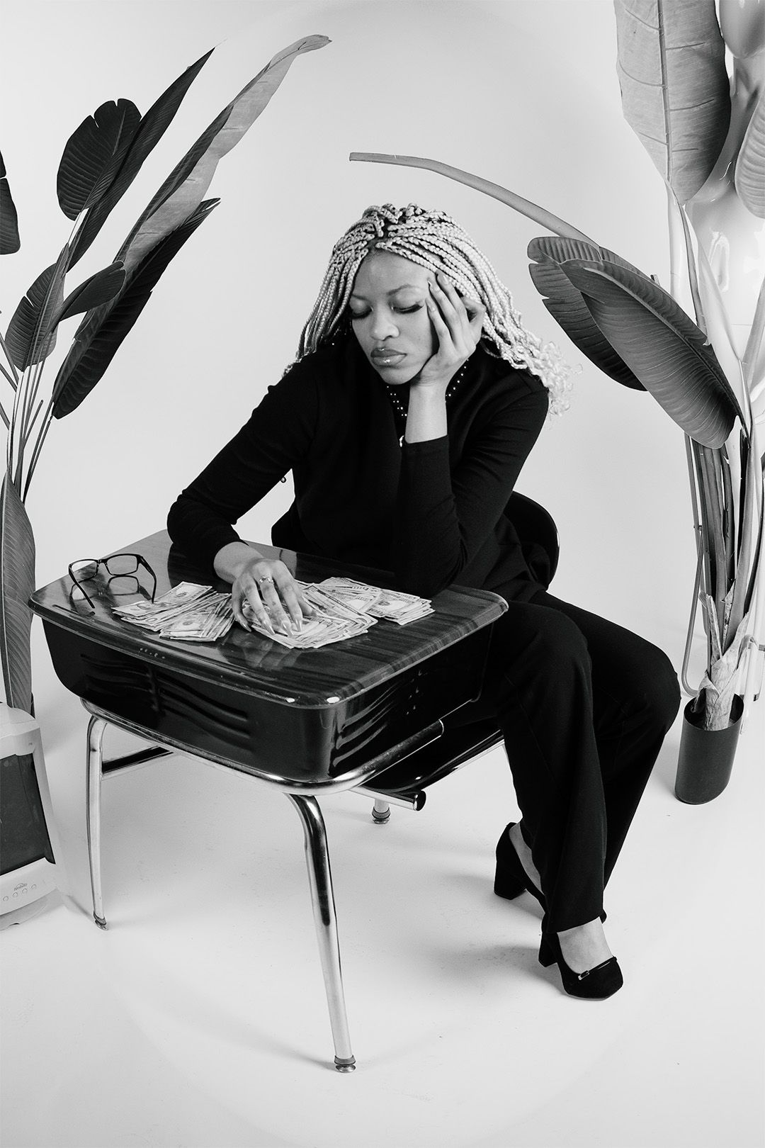 Black and white photo of a woman with braids sitting at a vintage desk with cash, looking stressed.