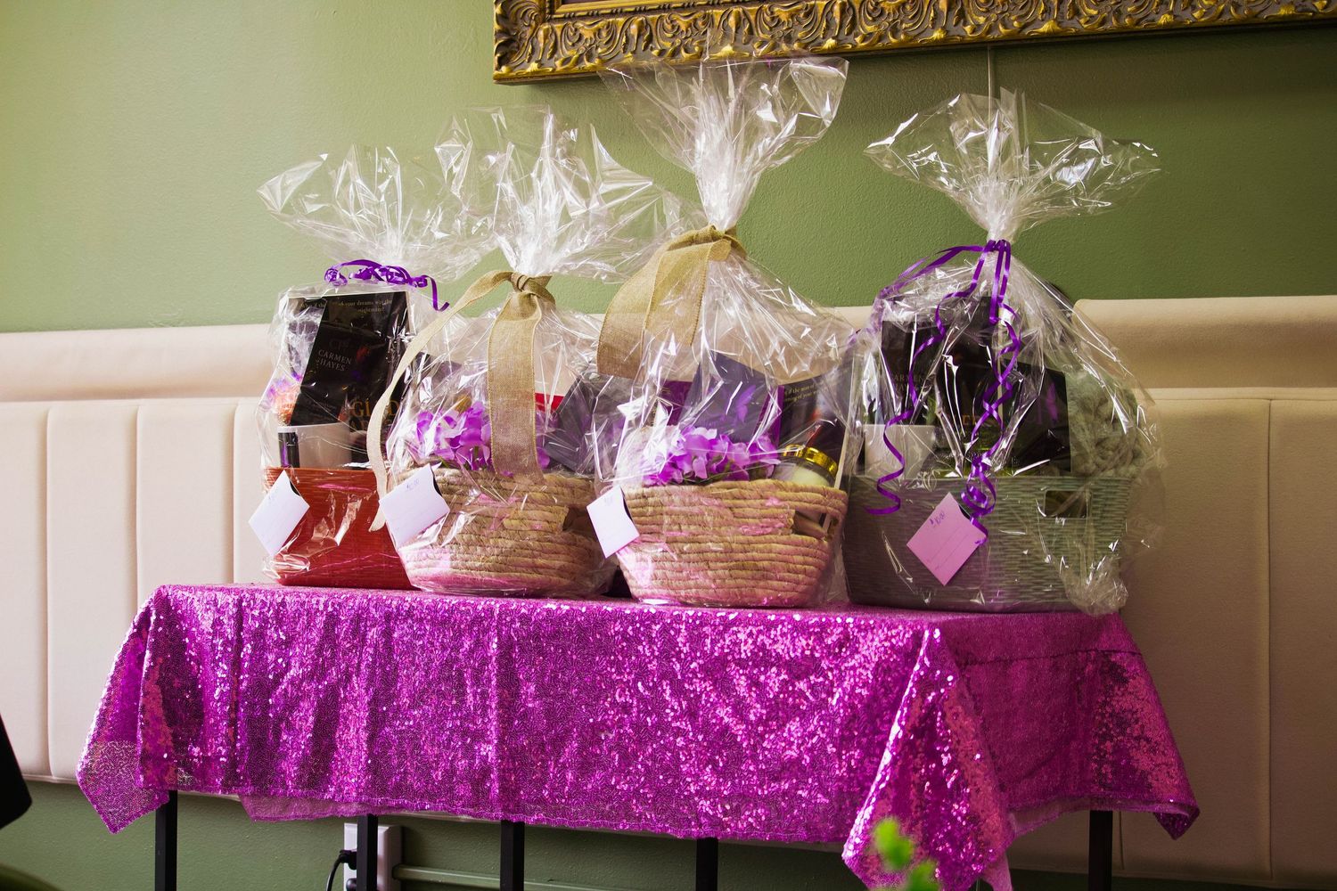 Three decorative gift baskets wrapped in cellophane displayed on a purple sequin tablecloth at an event.