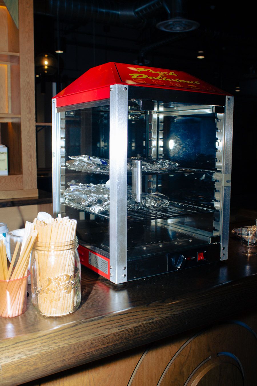 Red and chrome heated food display case on a restaurant counter with wooden skewers.