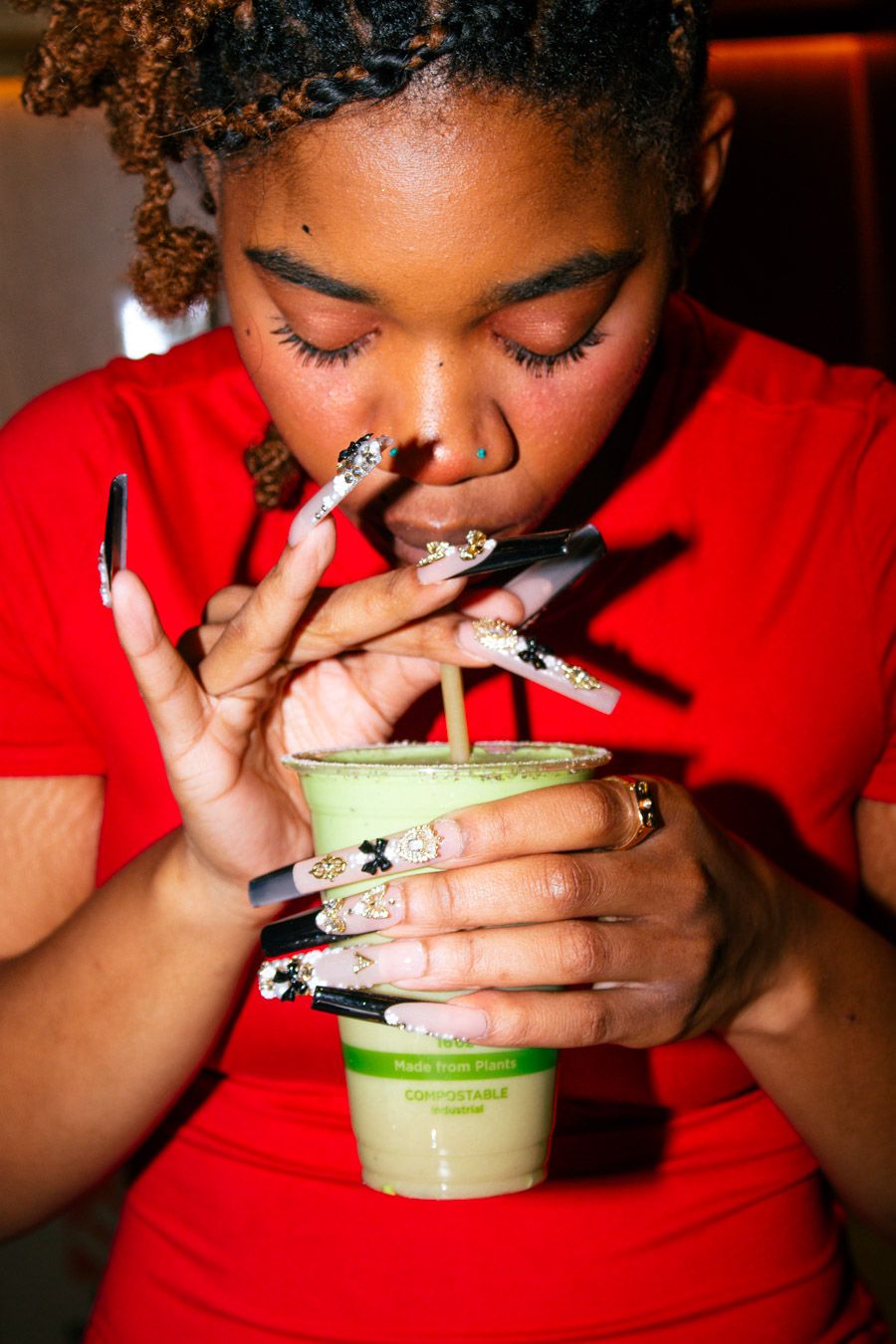 Woman with long decorated nails sipping a green matcha drink from a compostable cup.