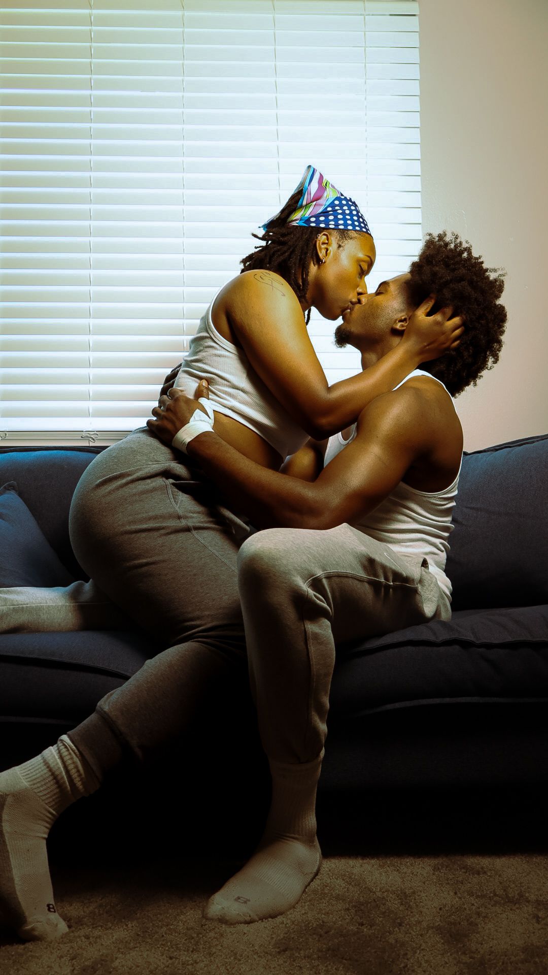 A couple shares a passionate kiss while embracing on a cozy blue sofa at home.
