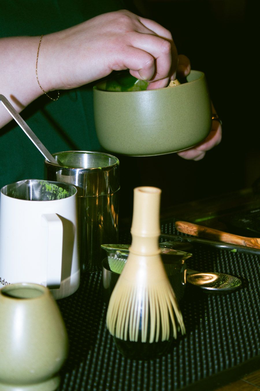 Hands preparing matcha tea with a bamboo whisk and traditional matcha tools.
