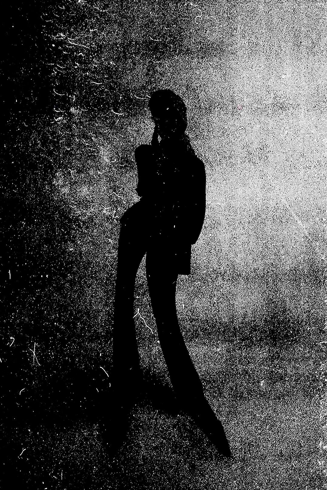 High-contrast black and white silhouette of a woman in flared pants standing against a textured background.