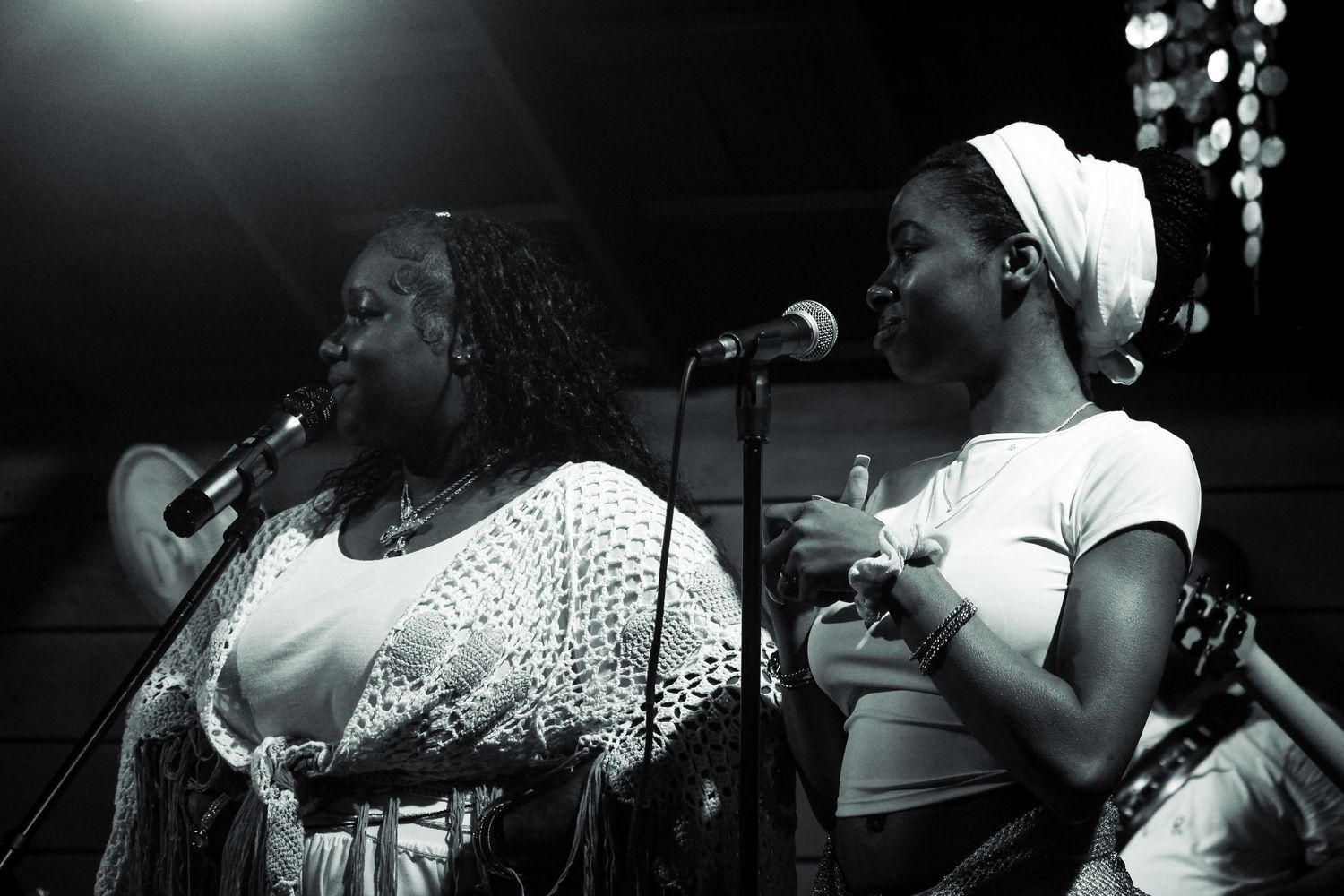 Two women perform on stage with microphones in a black and white concert photo.