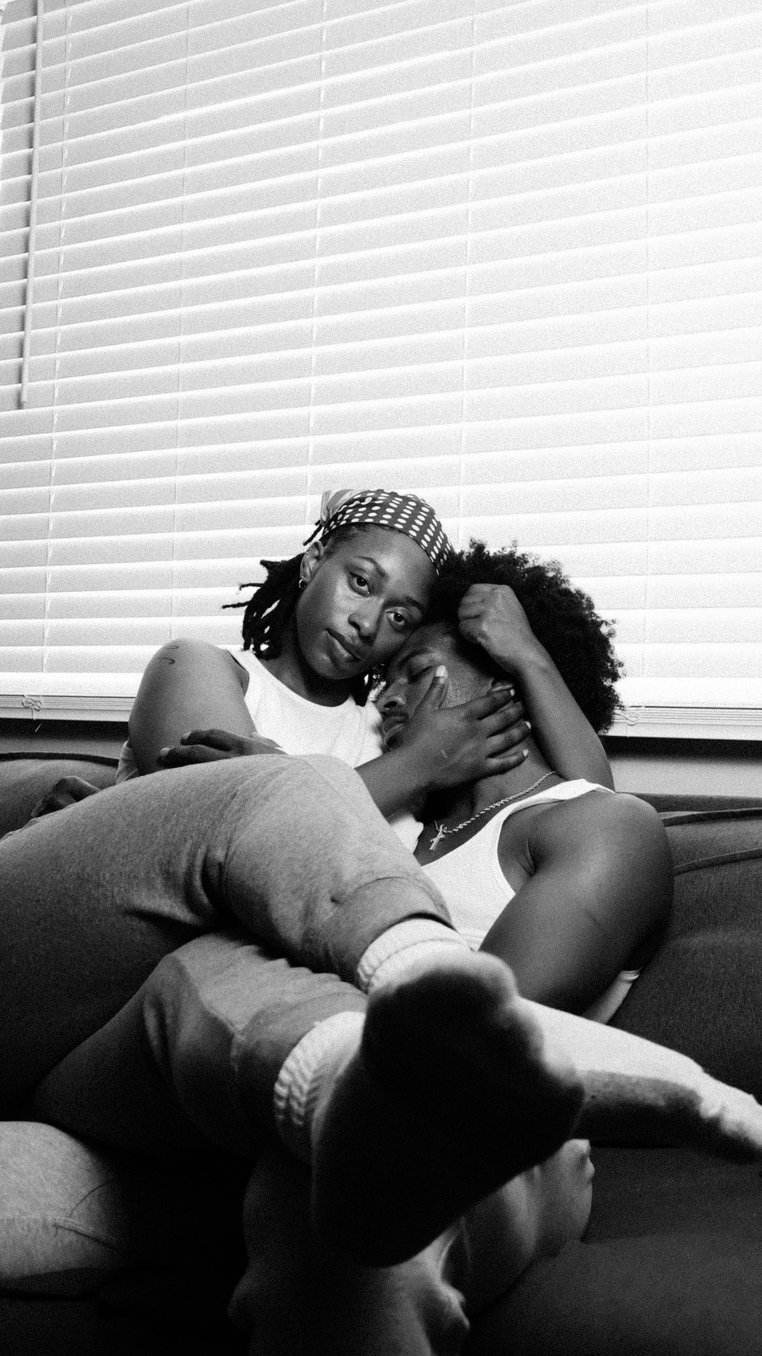 Black and white photo of a couple cuddling on a couch, woman resting her head on mans chest.