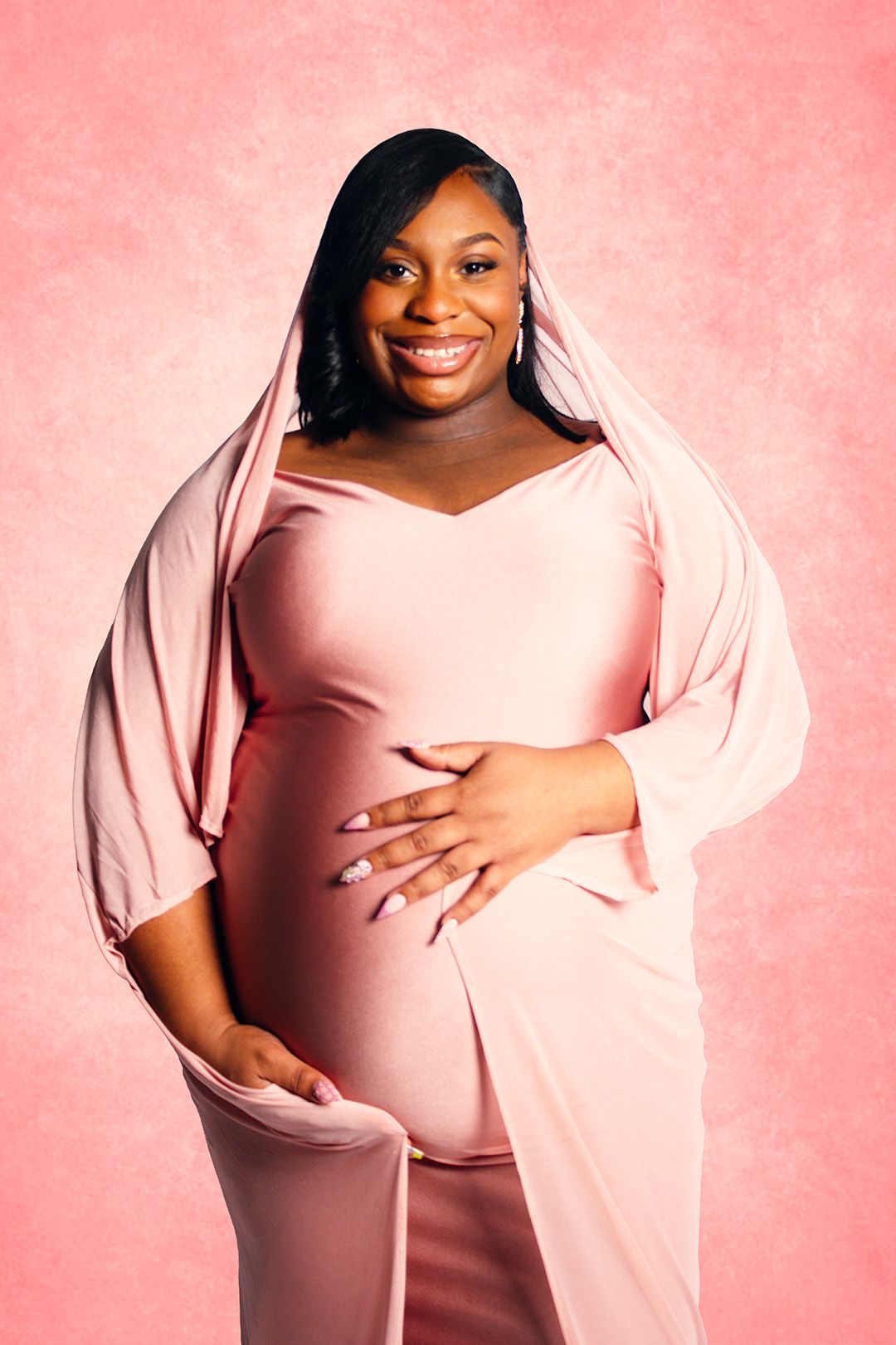 Smiling pregnant woman in a pink off-shoulder maternity gown posing against a pink backdrop.