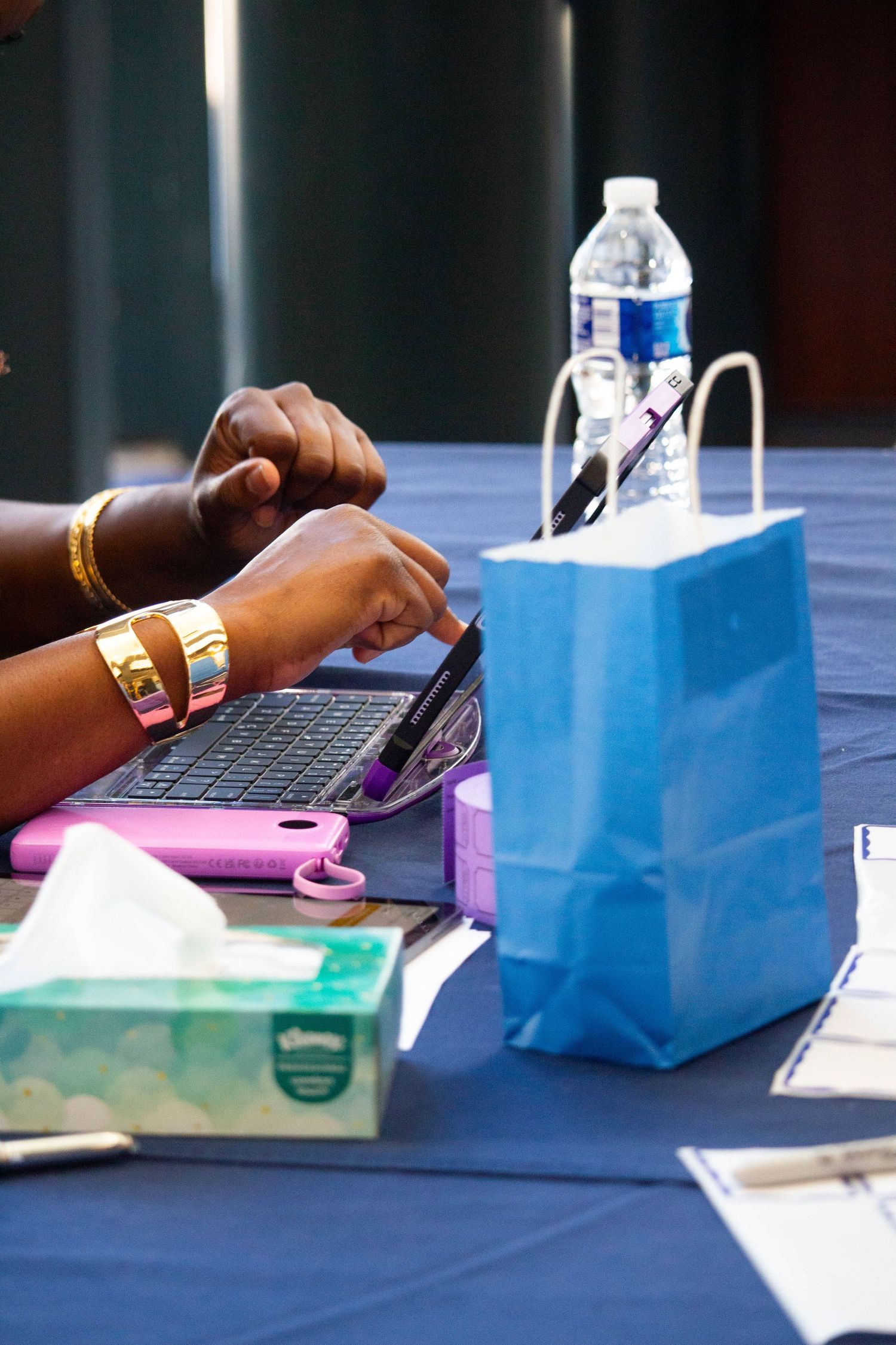Close-up of hands using a tablet at a registration table with a blue gift bag and water bottle.