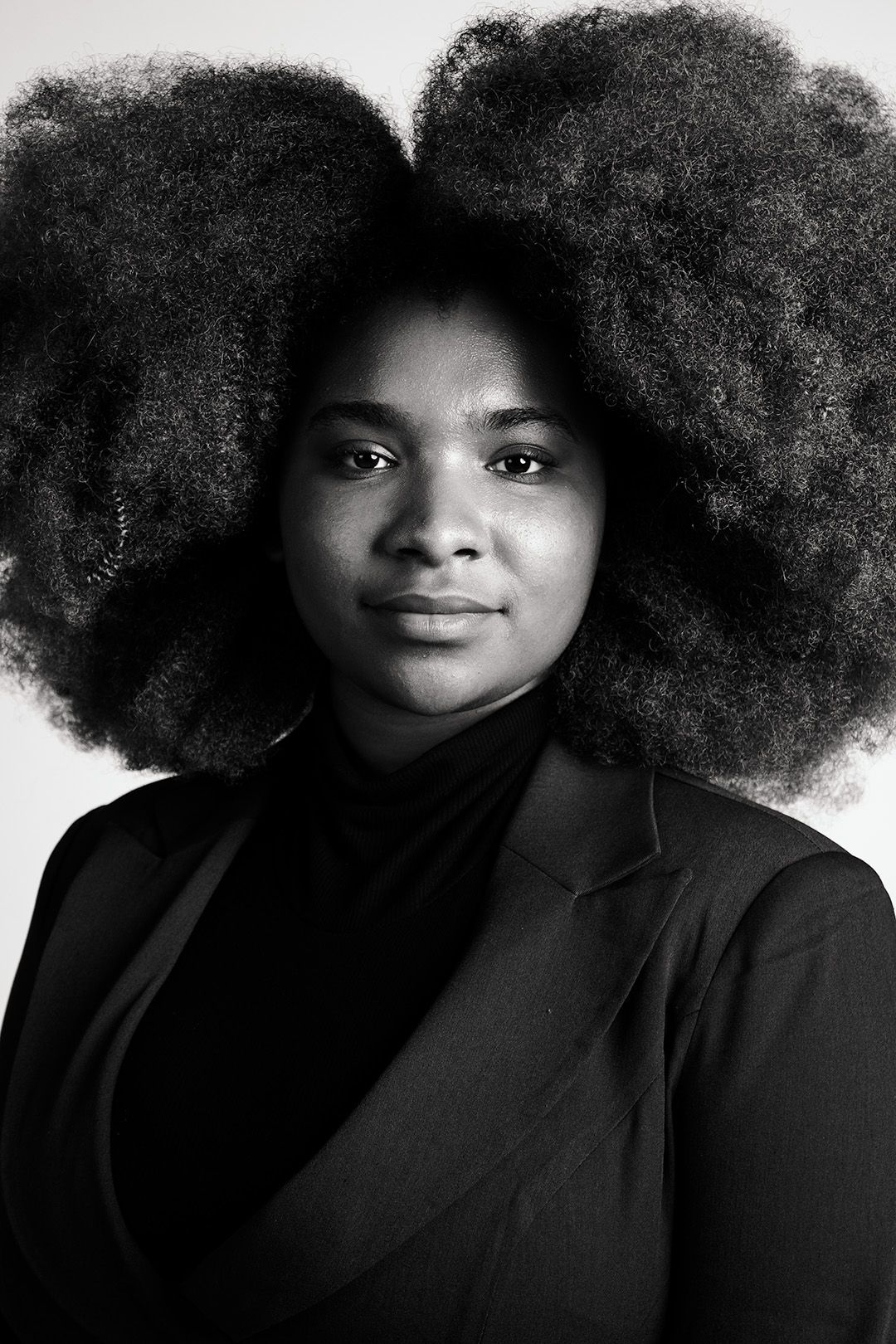 Black and white portrait of a young woman with voluminous natural afro hair wearing a black blazer.