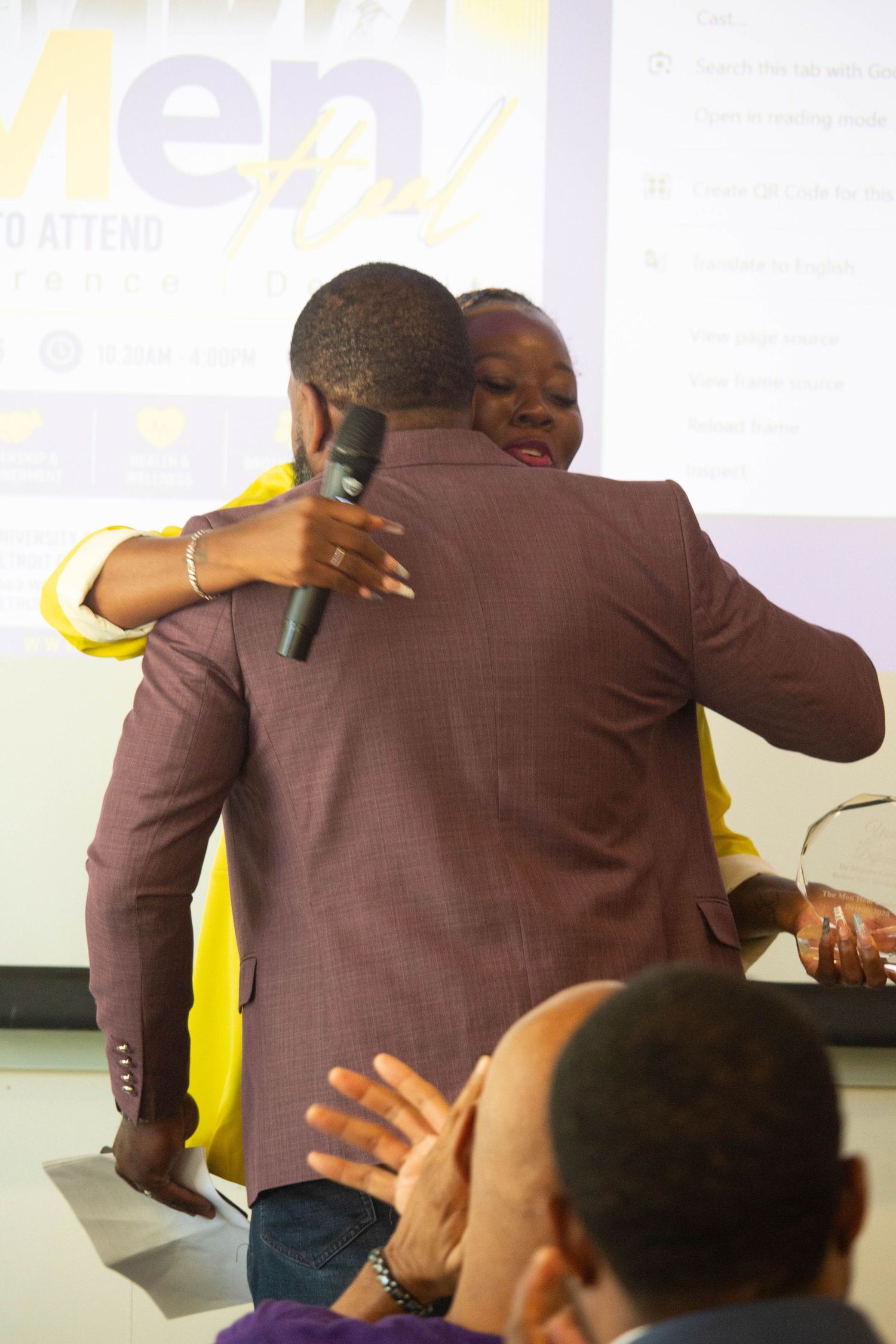 Two people sharing a warm hug at a Men conference event while holding a microphone.