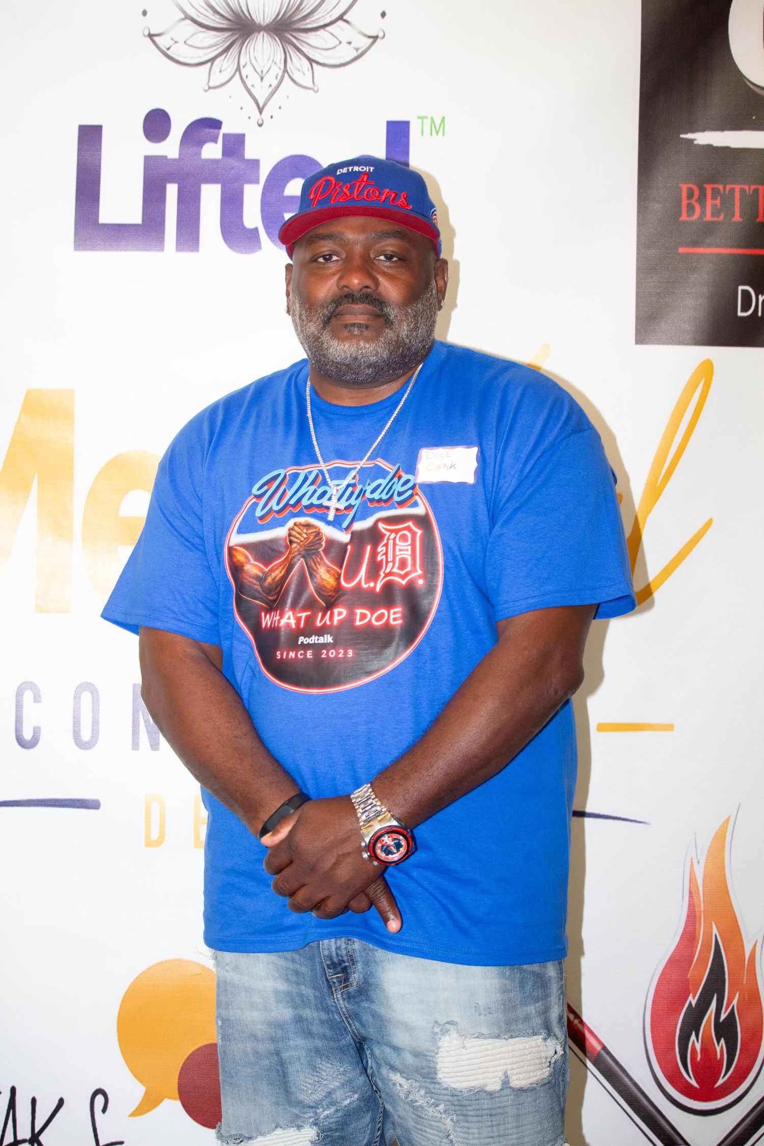 Man in blue Detroit Pistons t-shirt and cap posing at a Lifted event backdrop.