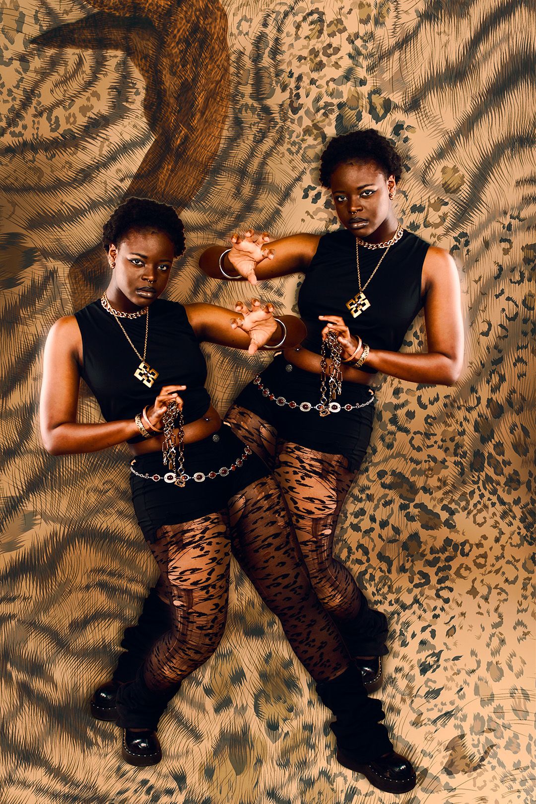 Two Black women in matching black tops, tiger-print tights, and gold jewelry pose against animal print backdrop.