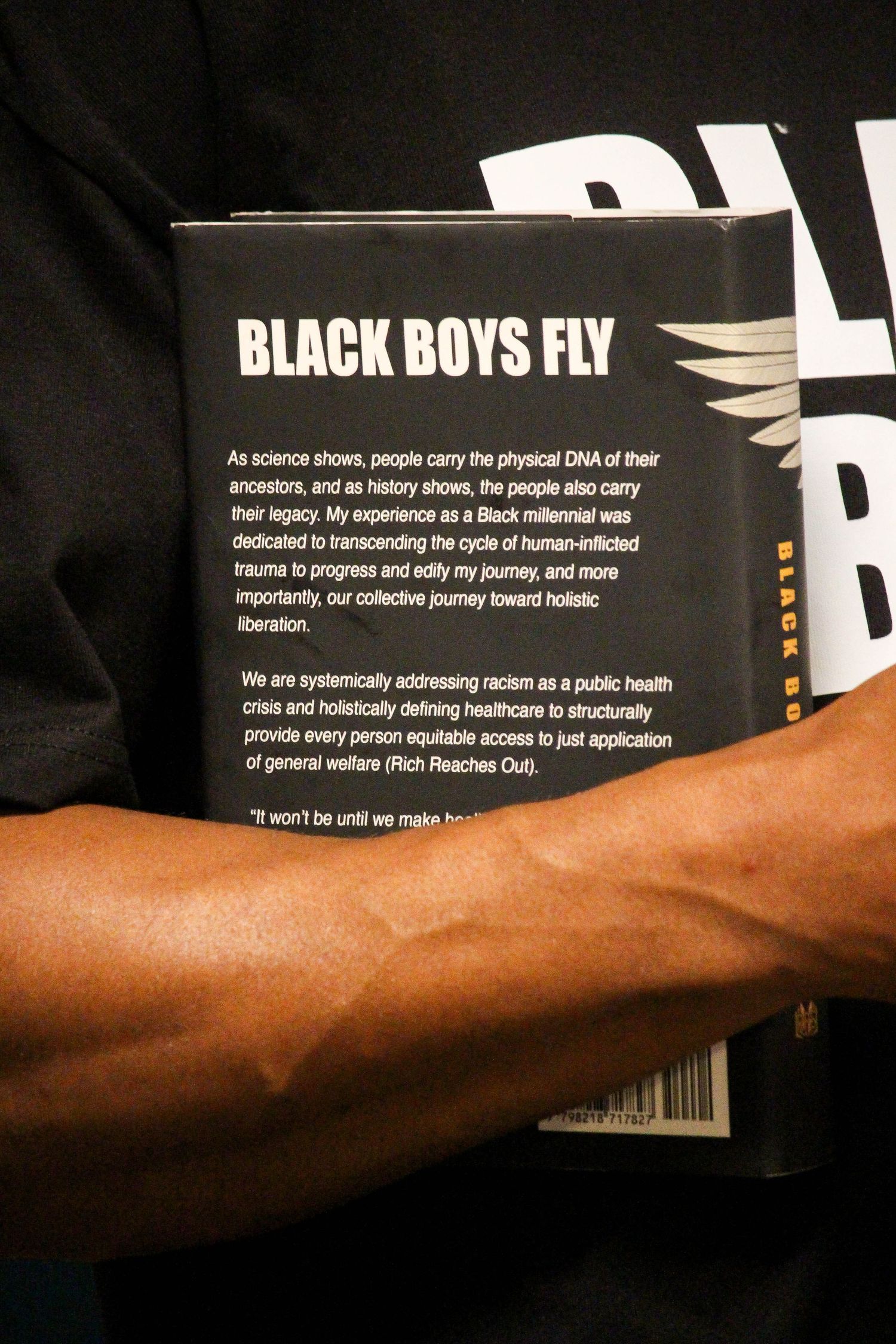 Person holding Black Boys Fly book showing back cover text about Black health and liberation.