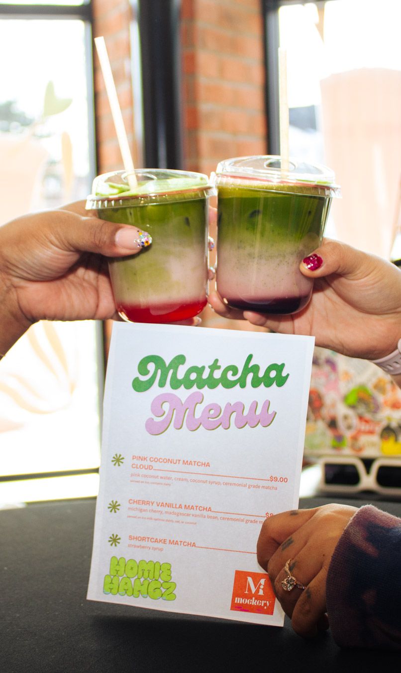 Two hands toasting with iced matcha drinks over a Matcha Menu card from Homie Hangz.