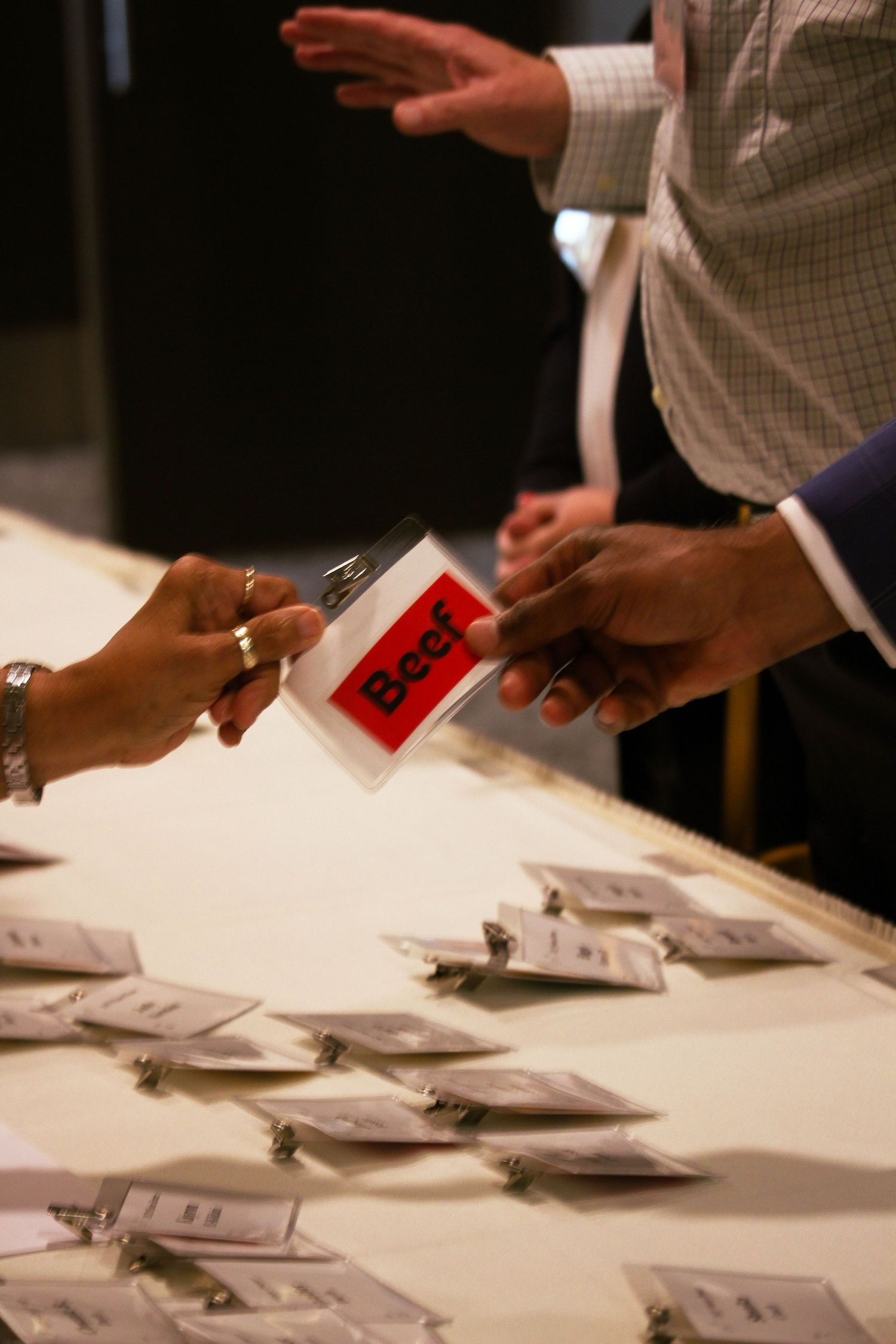 Hands exchanging a red Beef meal card at a white banquet table with name badges.