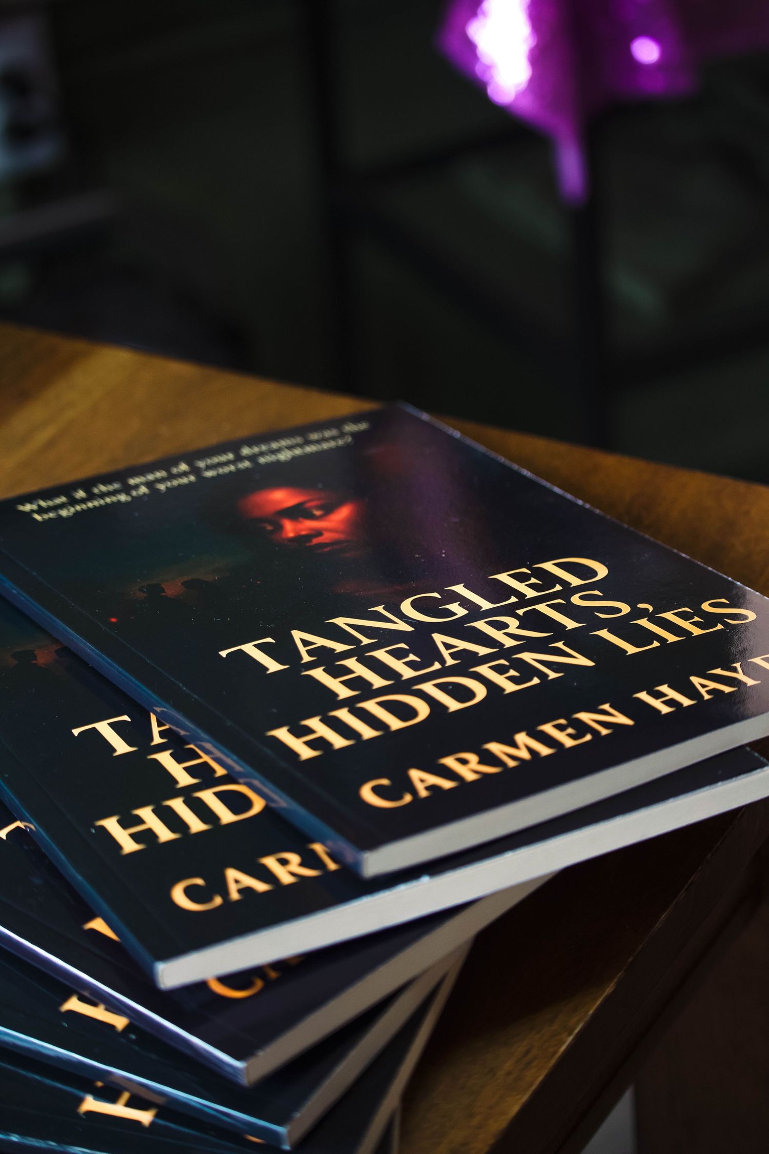 Stack of Tangled Hearts Hidden Lies books by Carmen Hayes displayed on a wooden table at a book signing.