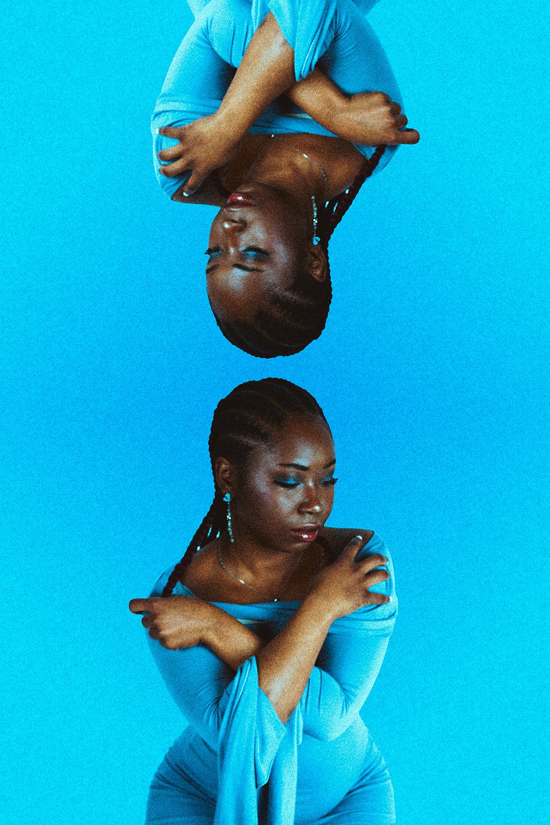 A Black woman in a blue outfit poses with arms crossed against a blue background, shown in a mirrored reflection.