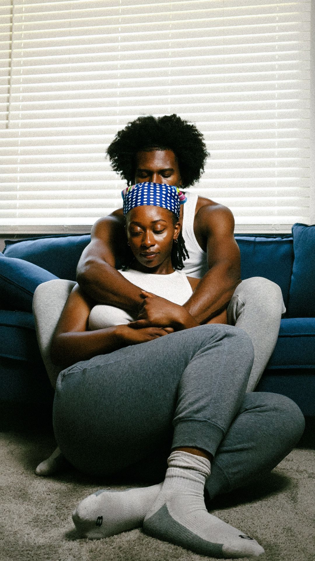 A couple embraces on the floor in front of a blue sofa, the man wrapping his arms around the woman tenderly.