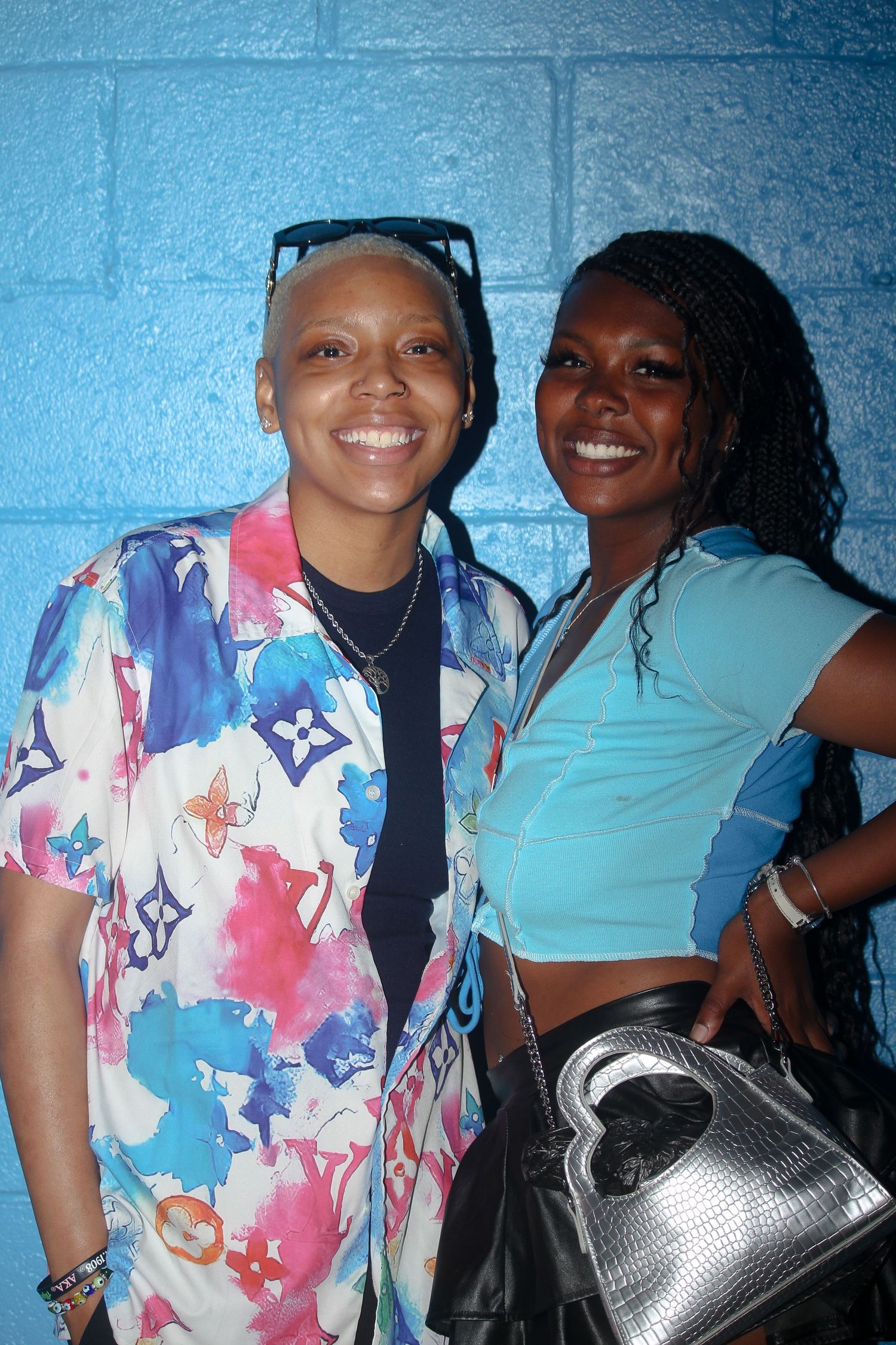 Two smiling women pose together against a blue wall, one in a Louis Vuitton print shirt.