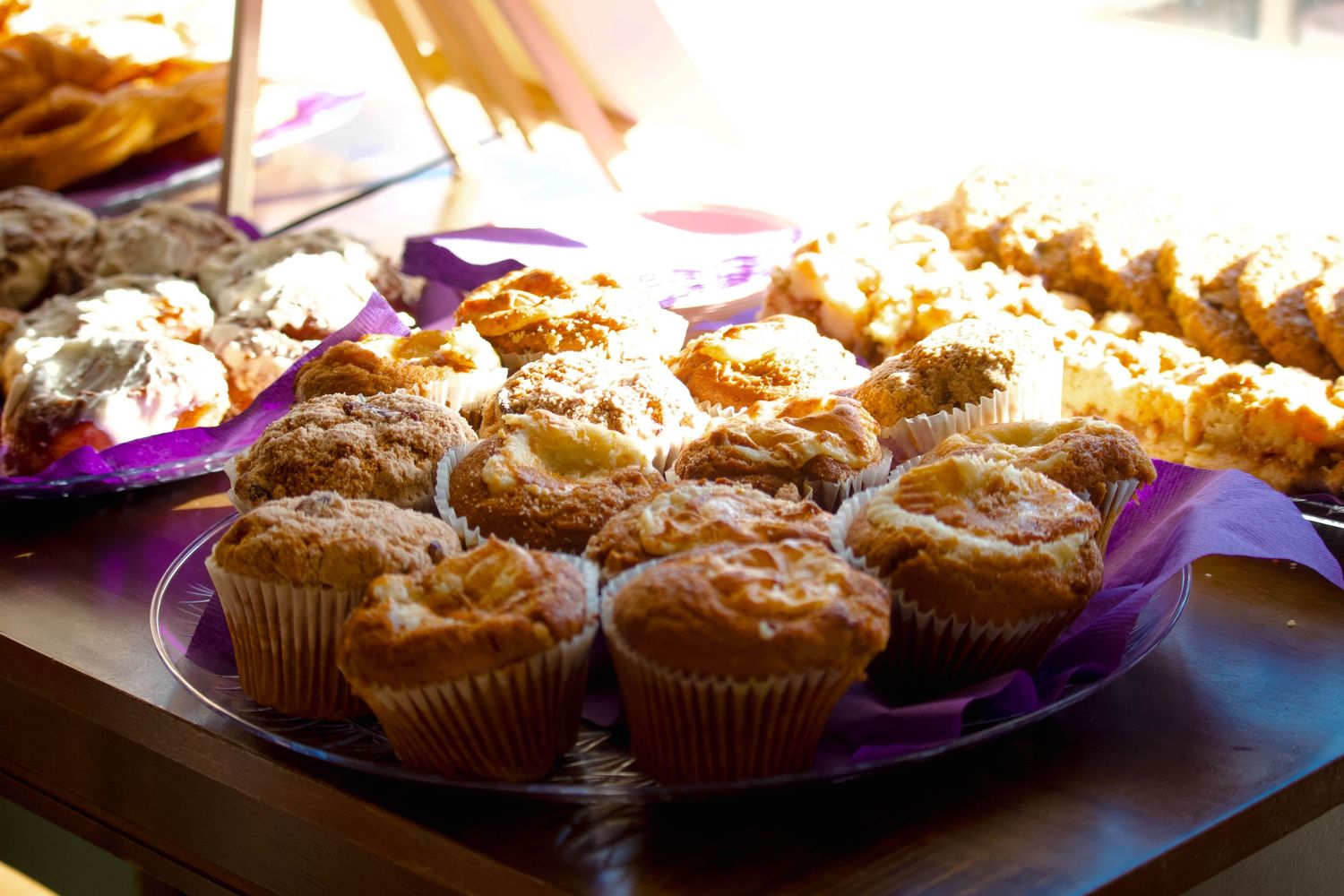 Assorted freshly baked muffins and pastries displayed on purple plates at a book signing event catering spread.