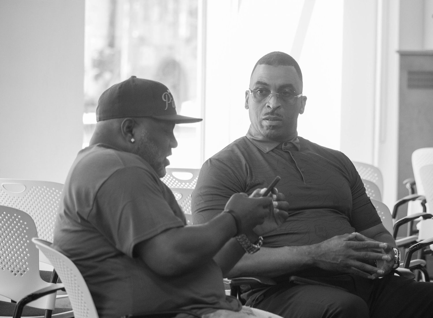 Two men in casual attire having a conversation while seated in chairs, captured in black and white photography.