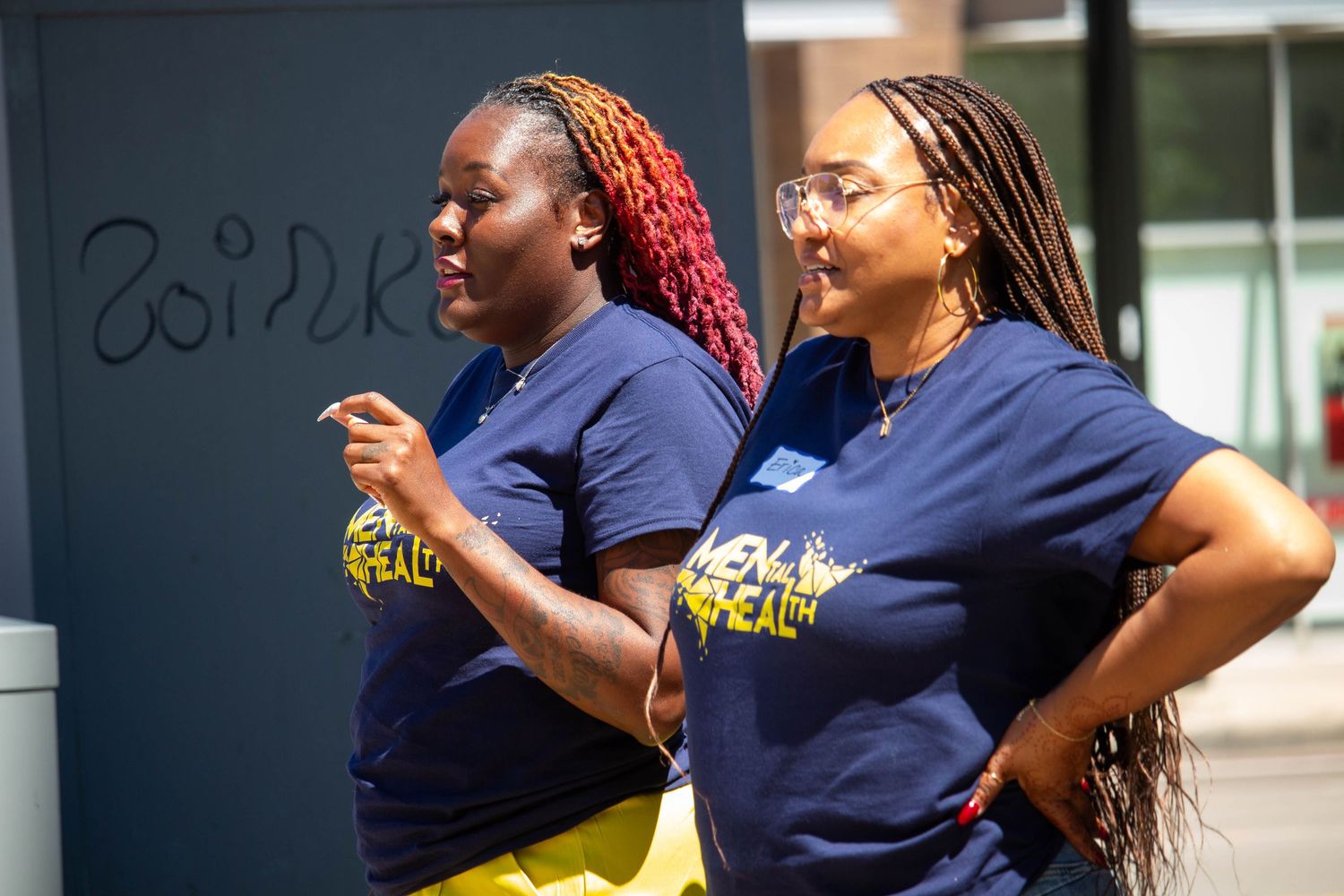 Two women wearing navy blue mental health awareness t-shirts standing outdoors at a community event.