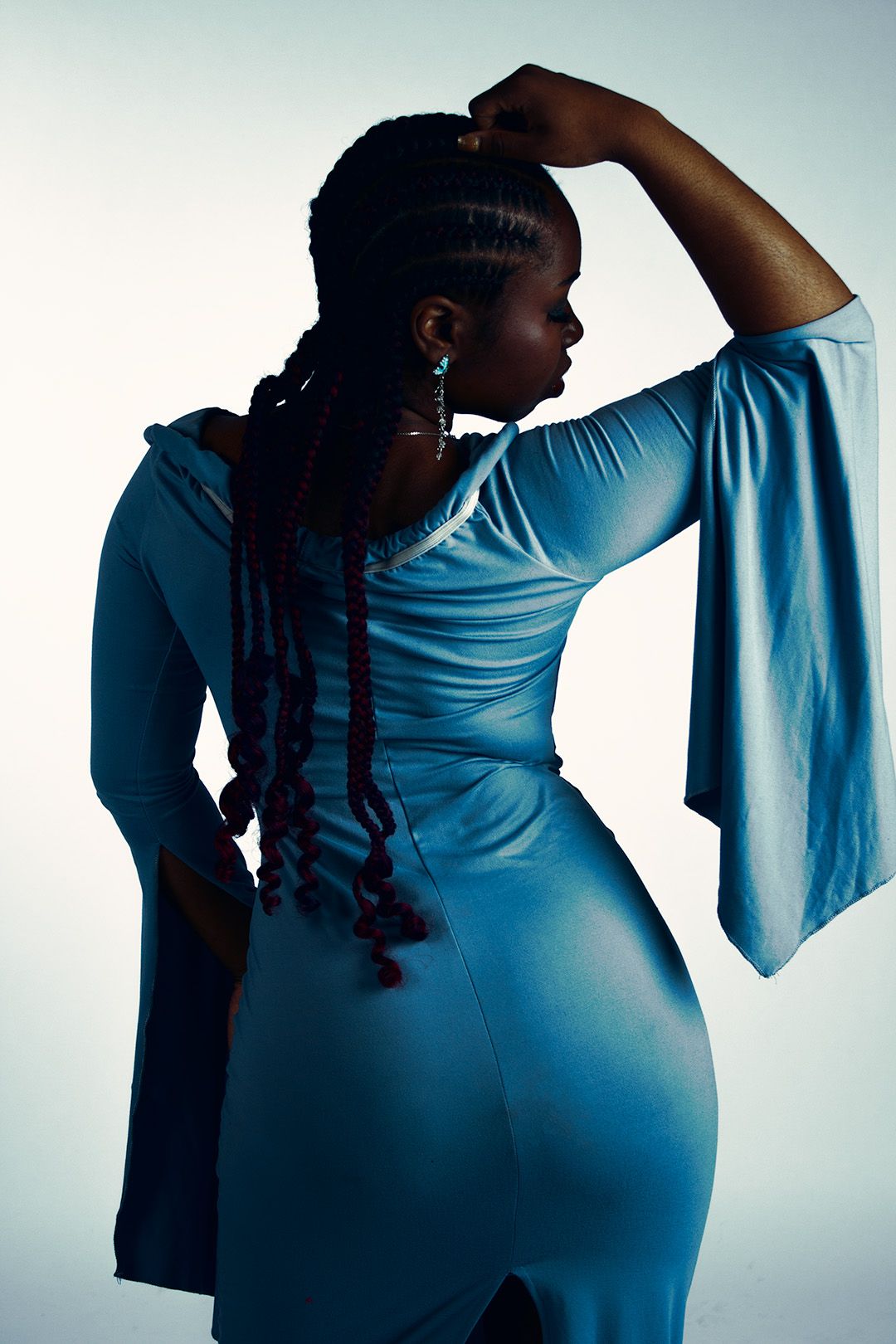 Black woman in blue dress with braids poses from behind showing off elegant bell sleeves and fitted silhouette.