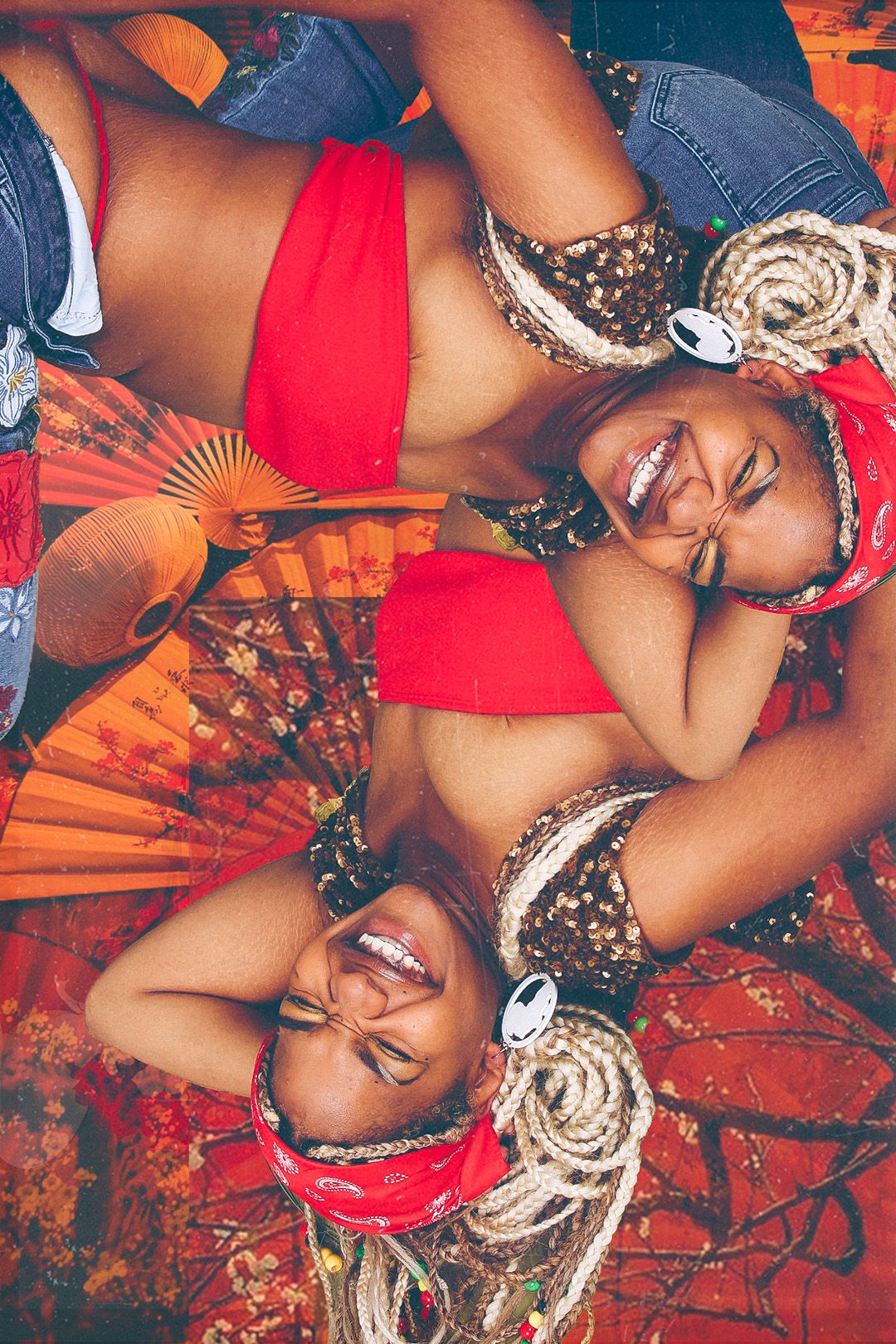 Two smiling women in colorful carnival costumes lying on a vibrant red and orange patterned background with decorative fans.