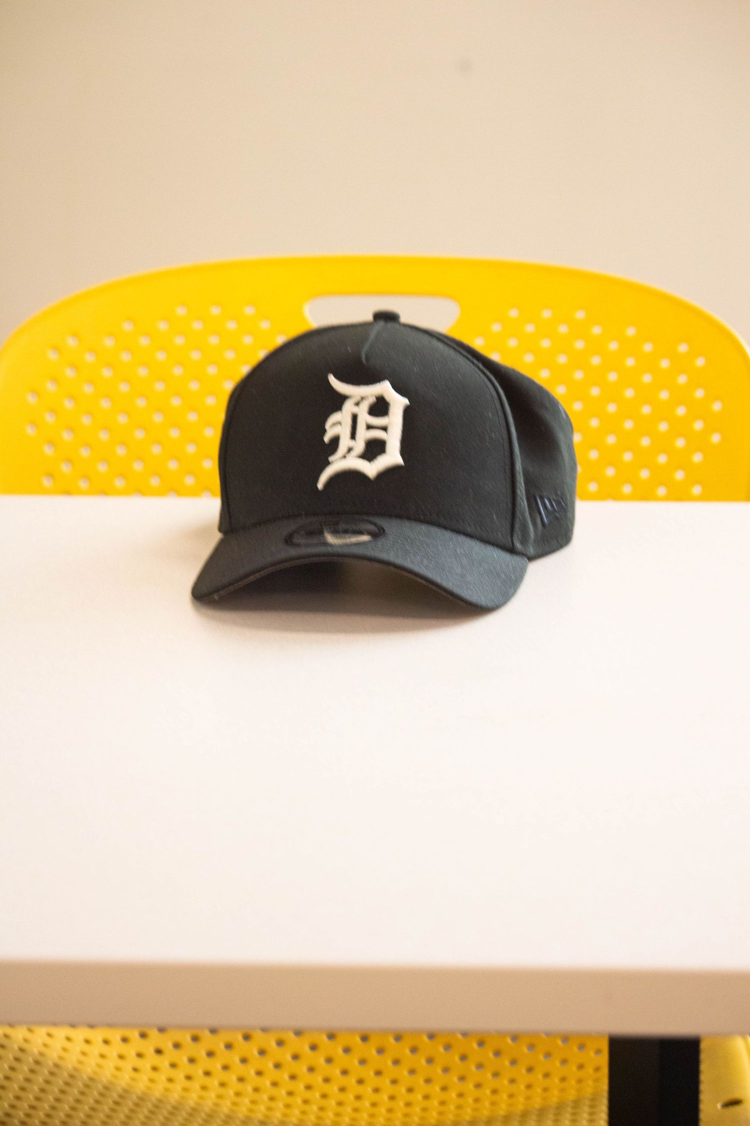 Detroit Tigers navy blue baseball cap placed on a white table with a yellow chair behind it.