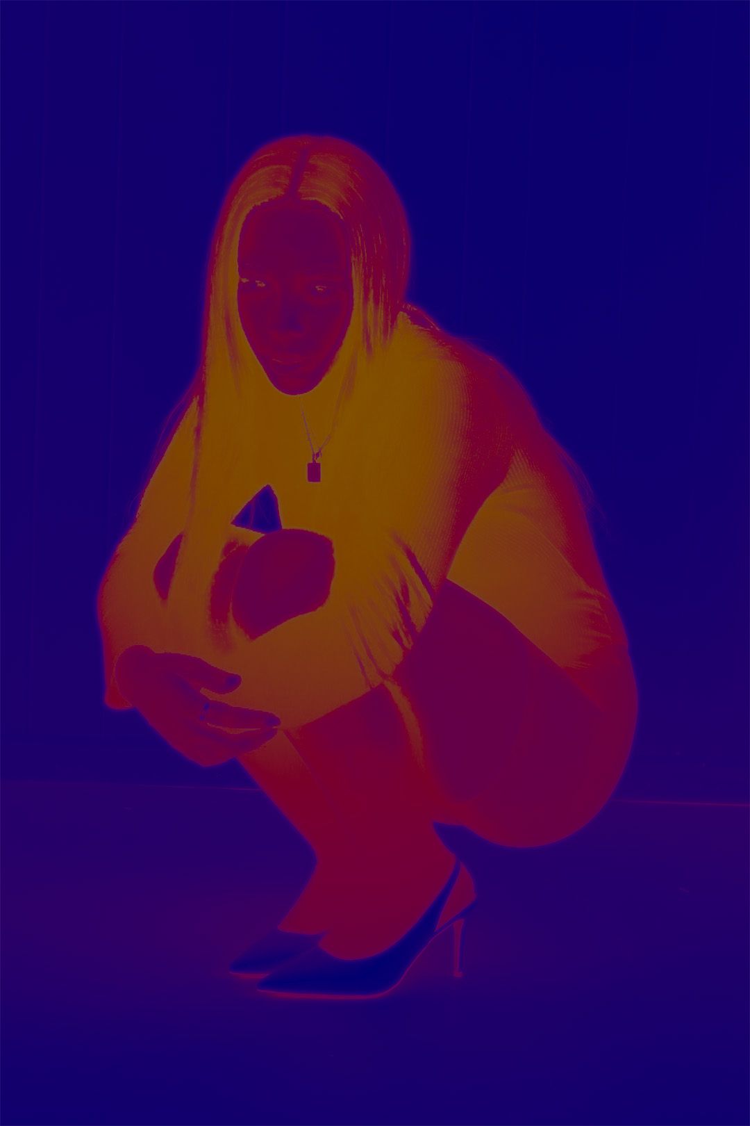 Woman crouching in dramatic red and blue thermal-style photography effect, wearing heels and holding a phone.
