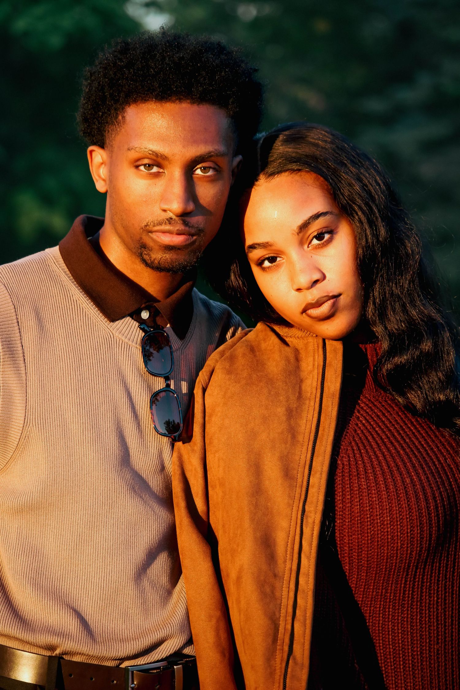 Close-up golden hour portrait of a stylish couple in earth-toned outfits looking at the camera.