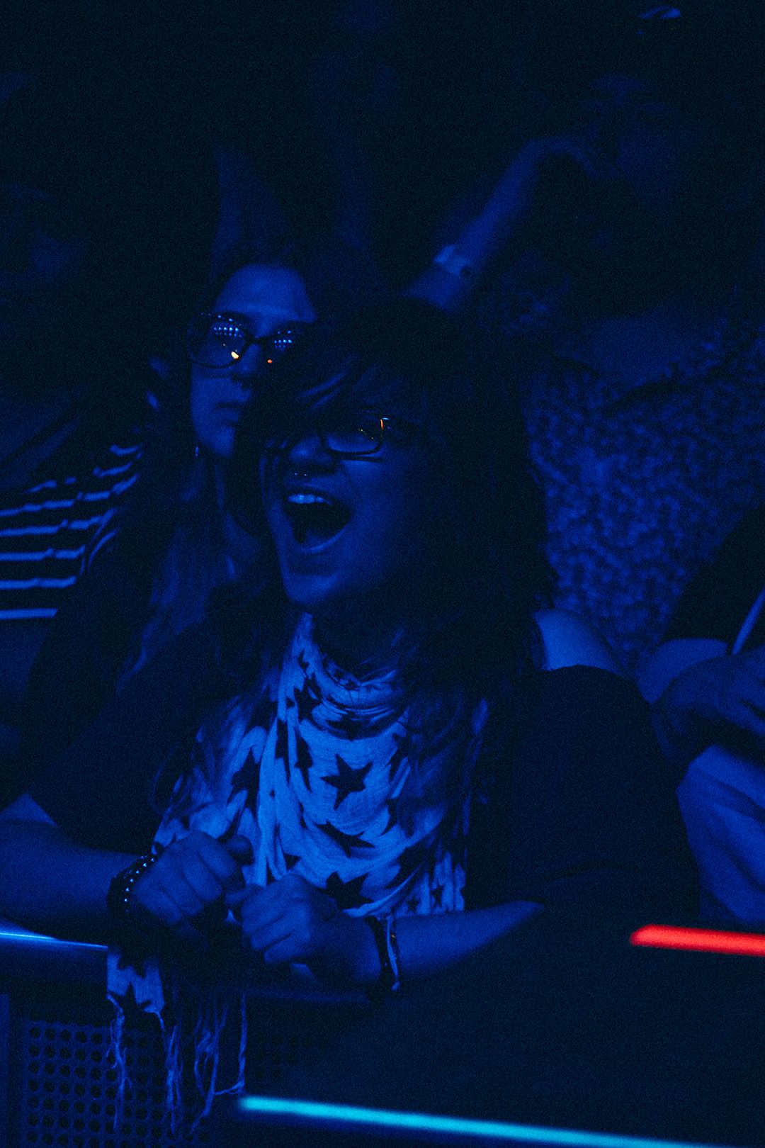 Excited concert fan in star-print shirt and glasses enjoys live show under blue neon lighting.