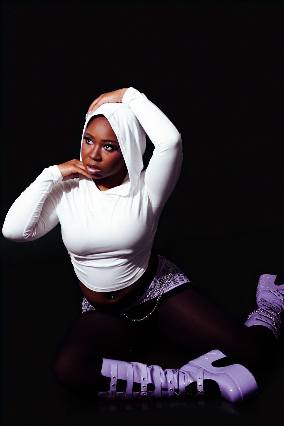 Woman in white crop top, snake print skirt, and purple platform boots poses against black background.