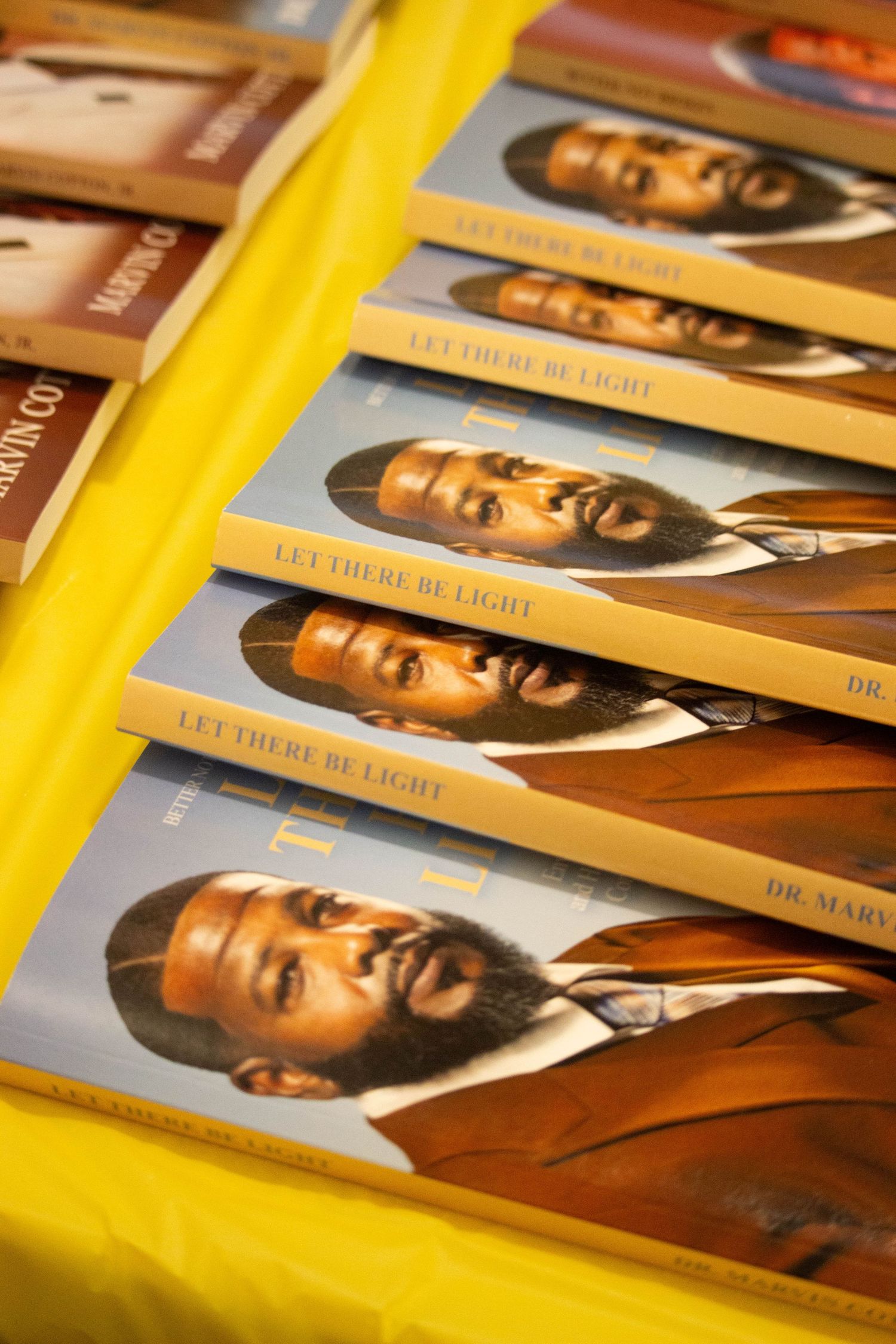 Copies of Let There Be Light by Dr. Marvin on a yellow tablecloth display.