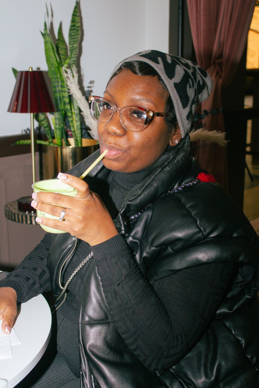 Woman in black puffer jacket and headscarf sipping green matcha through a straw.