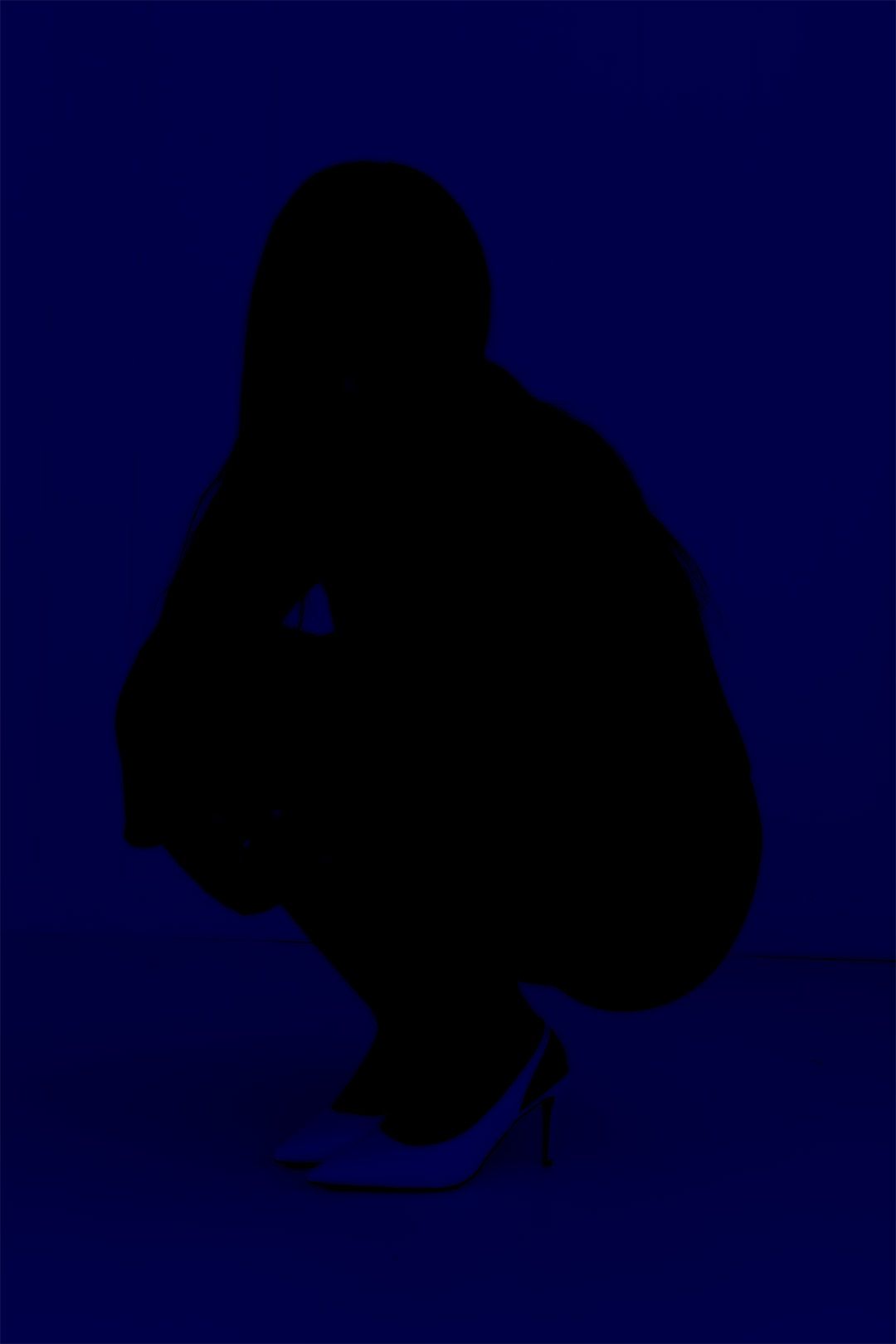 Silhouette of a crouching person in high heels against a deep blue background.