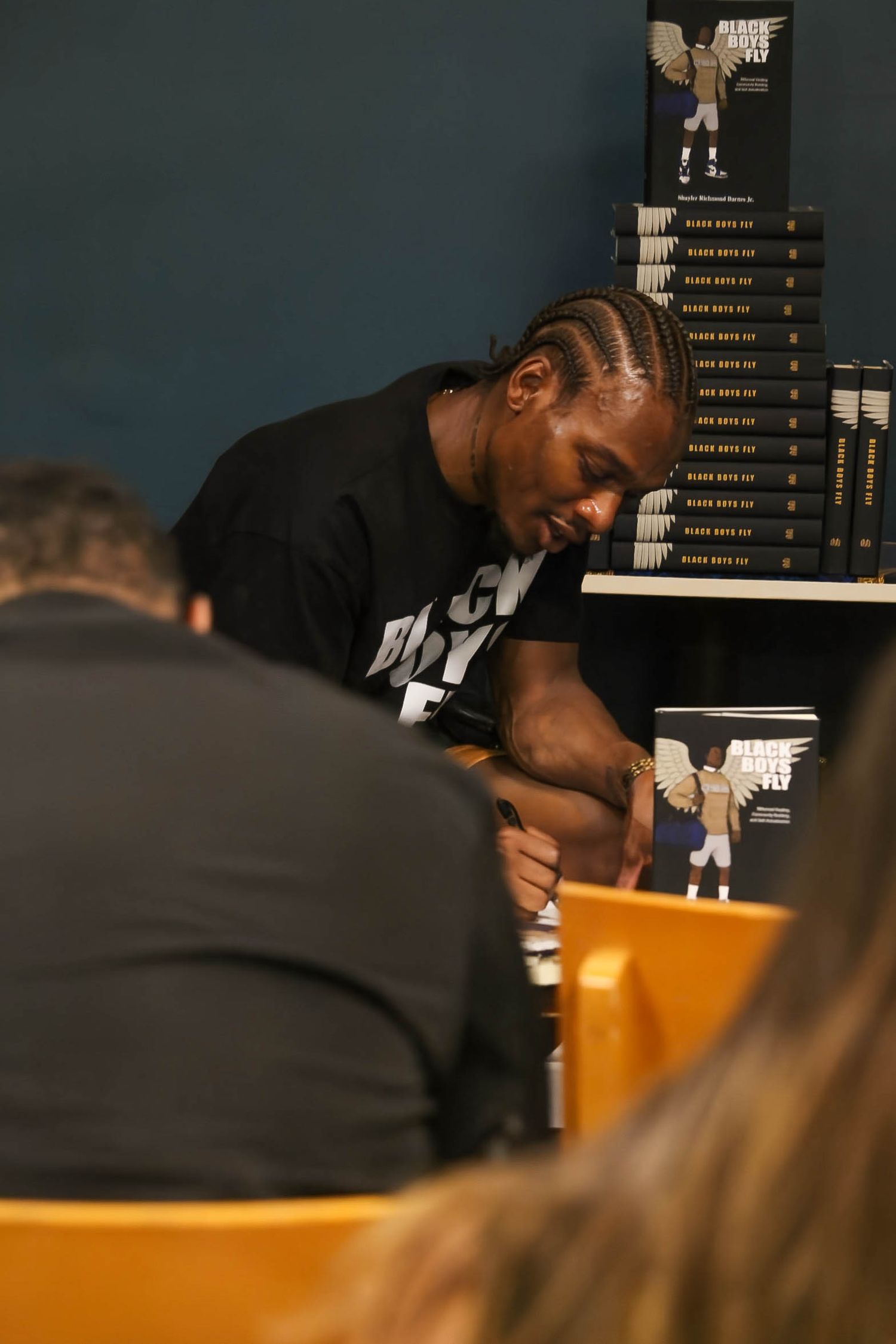 A man with braids signs copies of Black Boys Fly book at a signing event.