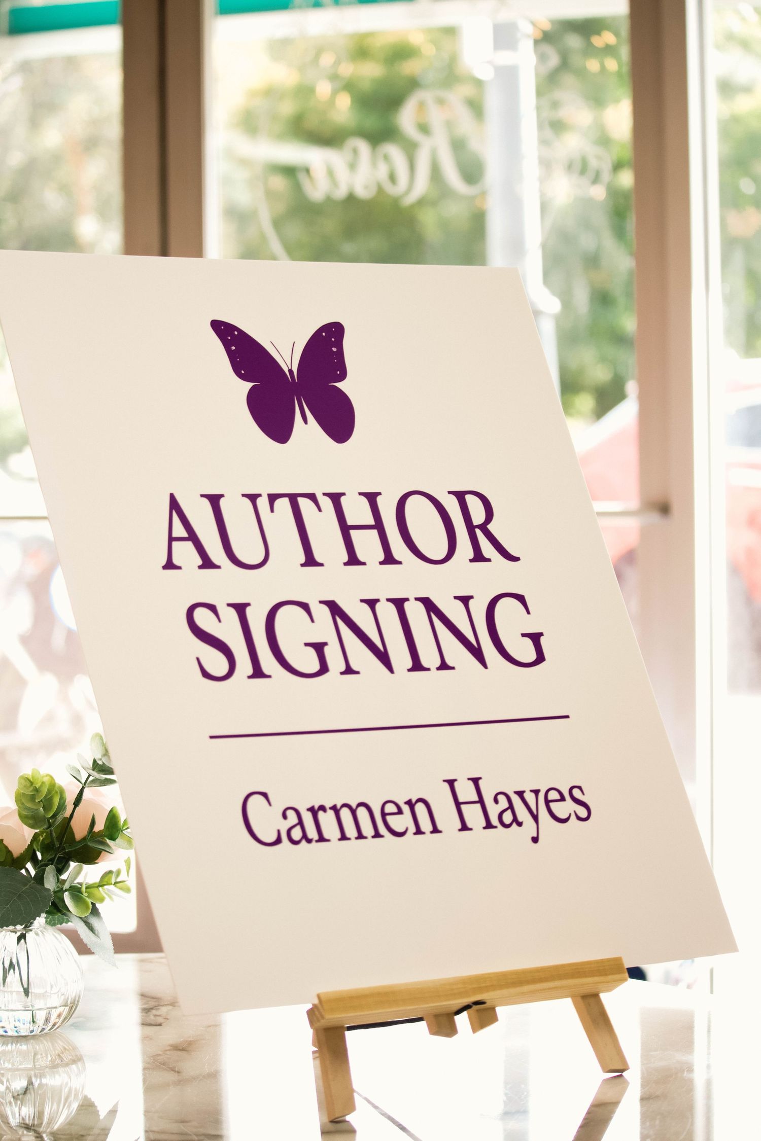 Author signing event sign for Carmen Hayes featuring a purple butterfly on a white board displayed on an easel.