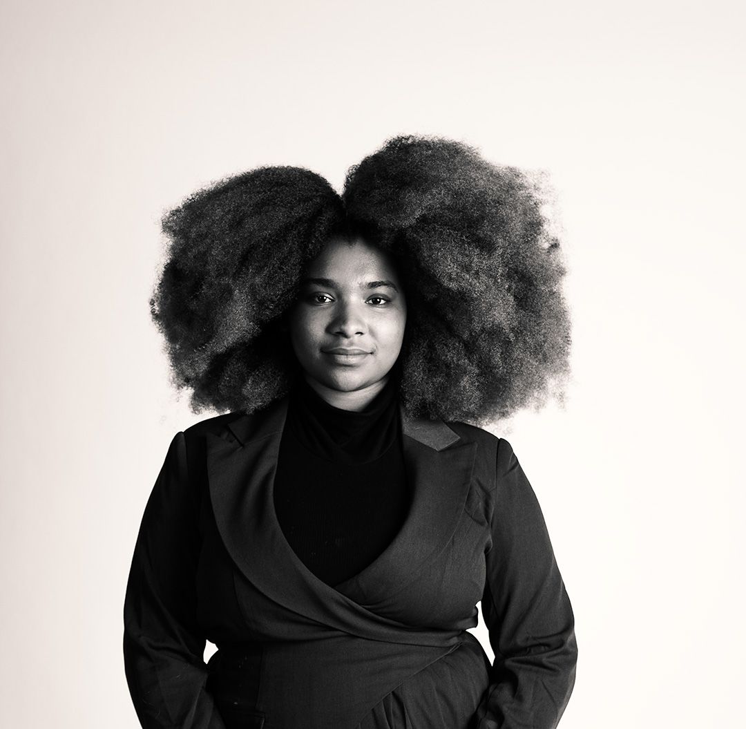 A black and white portrait of a woman with a large natural afro hairstyle wearing a black wrap top.