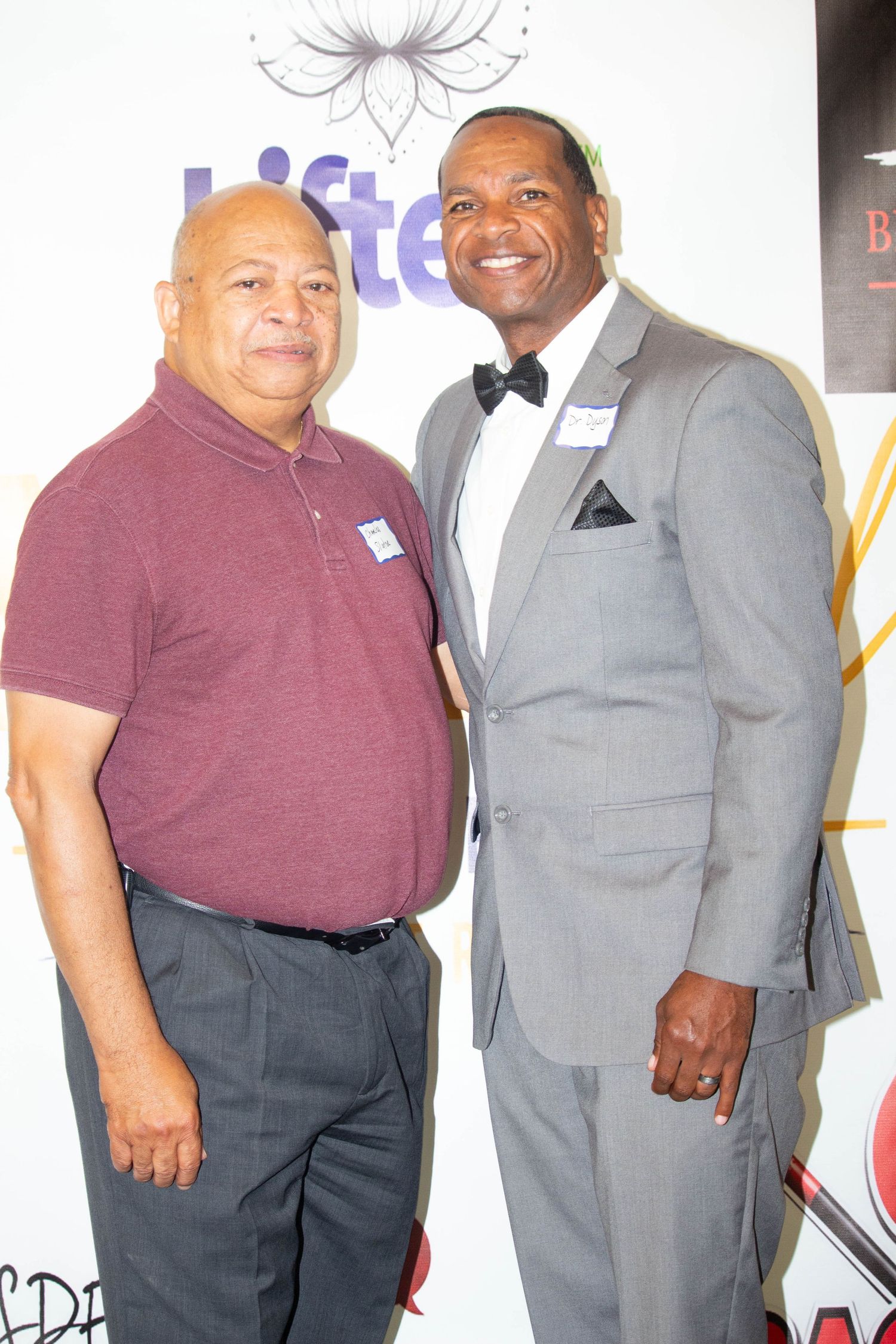 Two men posing together at a Lifted event, one in a maroon polo and one in a gray suit with bow tie.