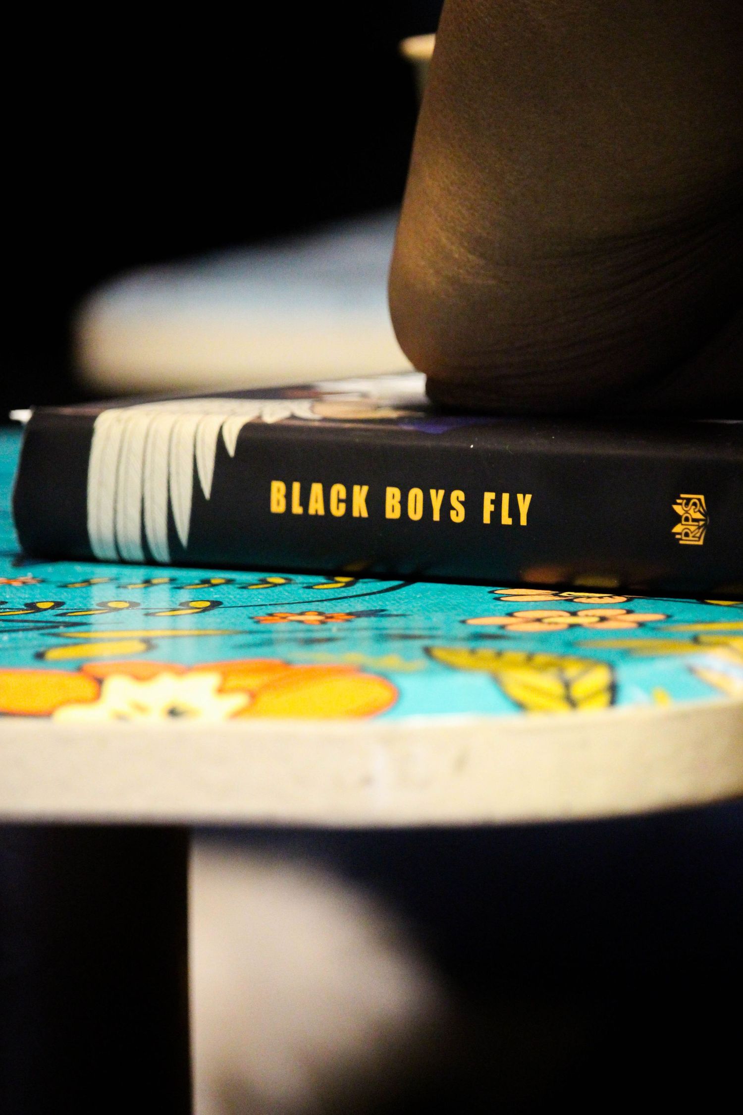 Black Boys Fly book with gold lettering spine resting on colorful butterfly table.
