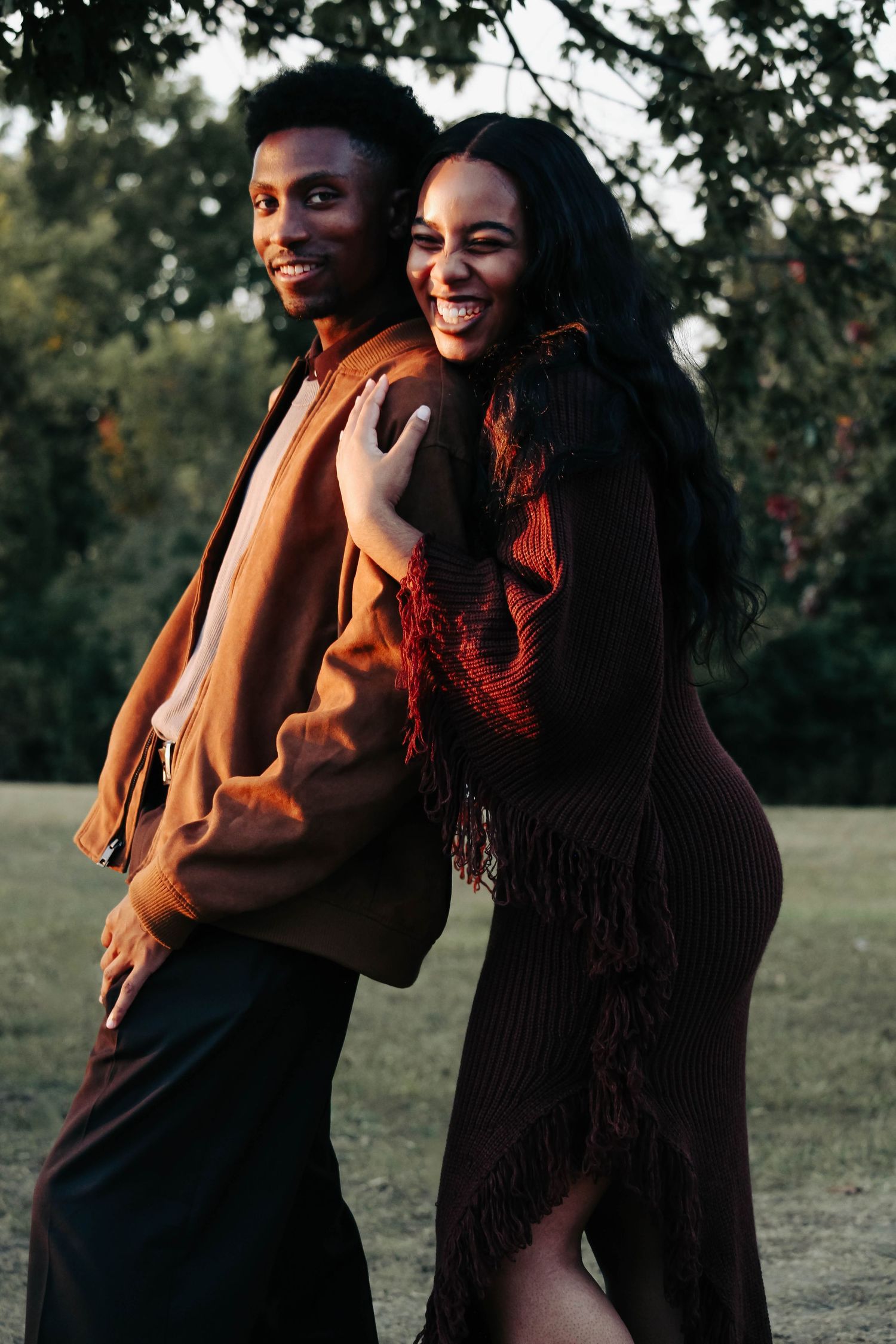 Outdoor photo of a laughing couple in warm earth-toned outfits standing back to back at sunset.