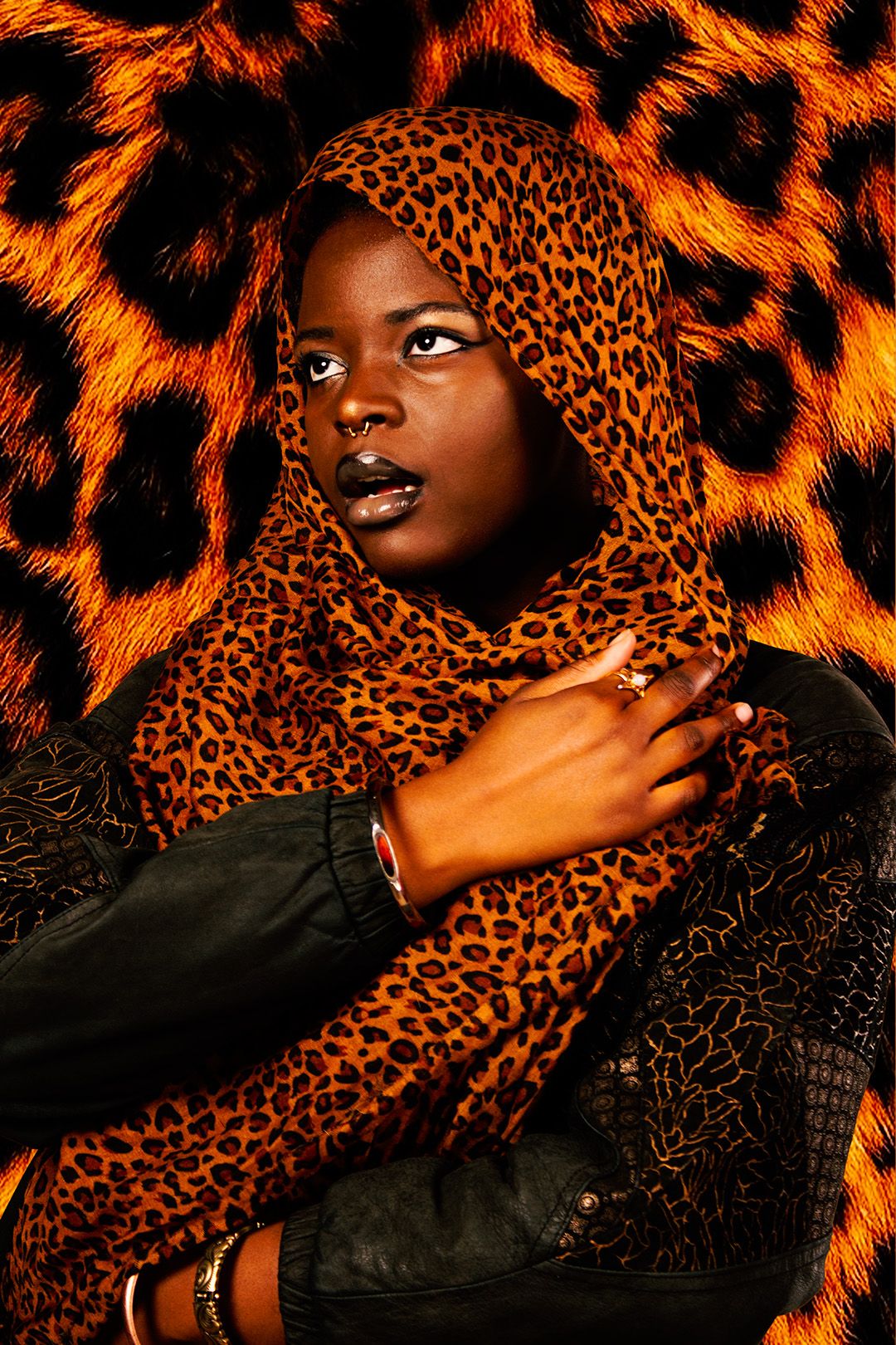 Woman wearing a leopard print hijab and black jacket against a leopard print background.