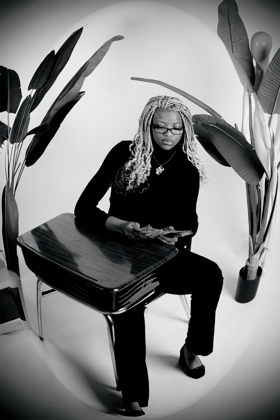 Black and white portrait of a woman with braids and glasses counting money at a retro desk.