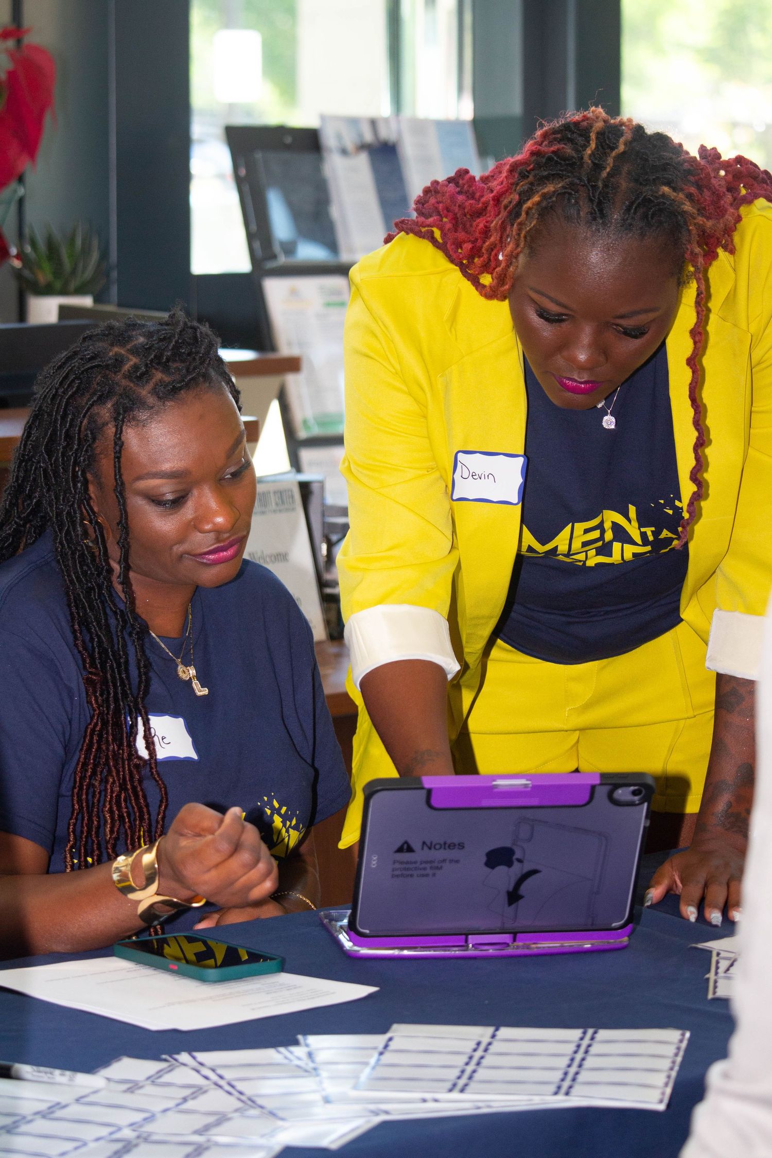 Two women collaborating over a tablet at a University of Michigan Men in Blue registration table.