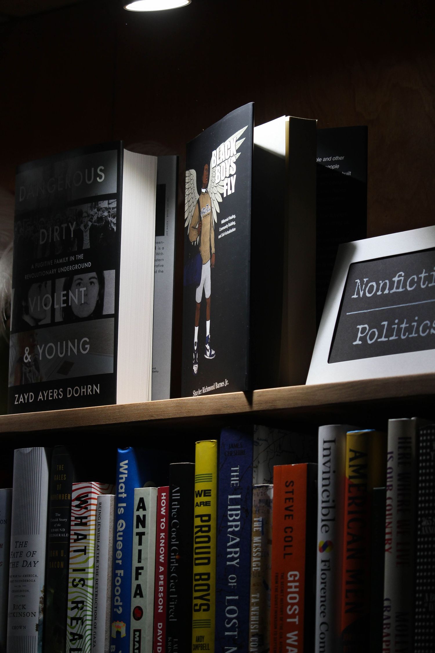 Bookshelf with nonfiction and politics books including The Proud Boys and Ghost War titles in a dimly lit library.