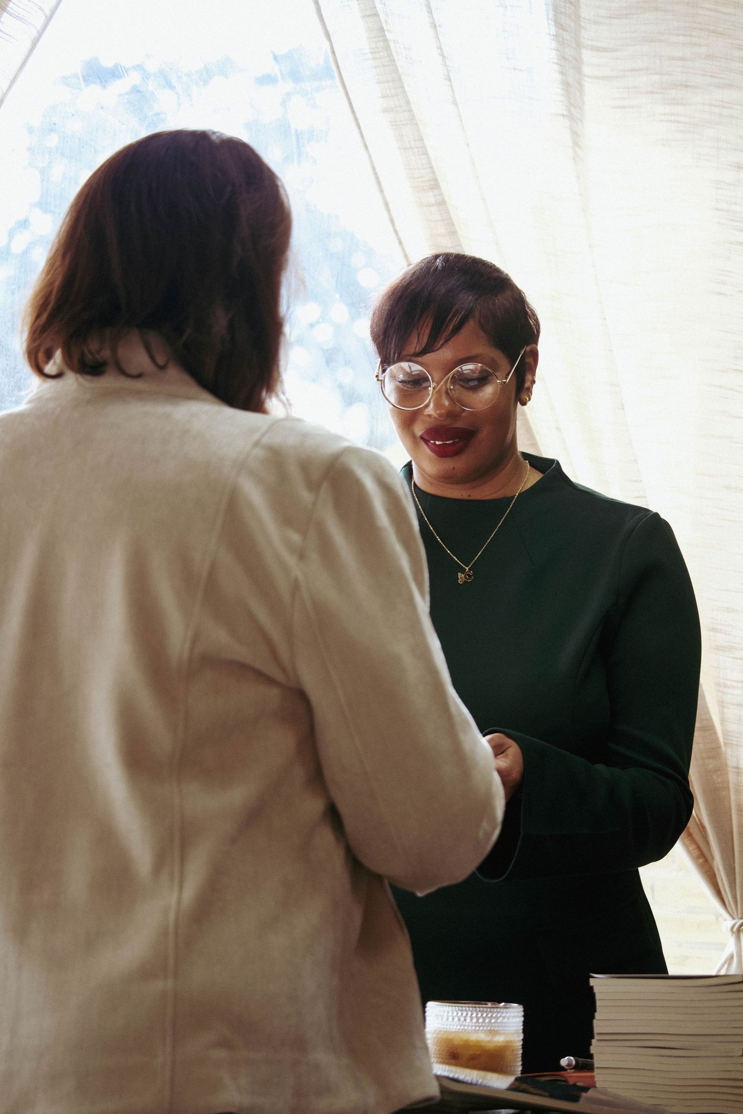 Author Carmen Hayes in green top and round glasses smiling while greeting a guest at her book signing event.