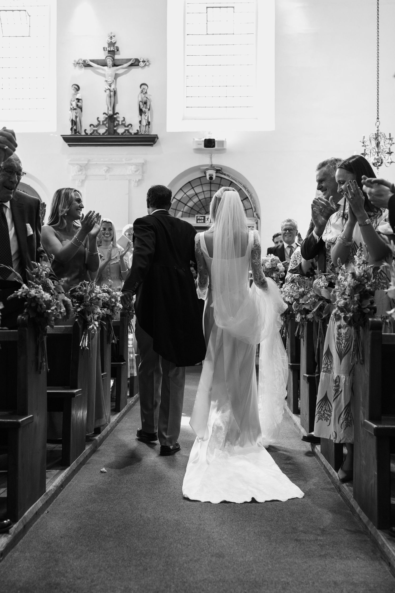 Black and white photo of bride and groom walking down the aisle of a church wedding.