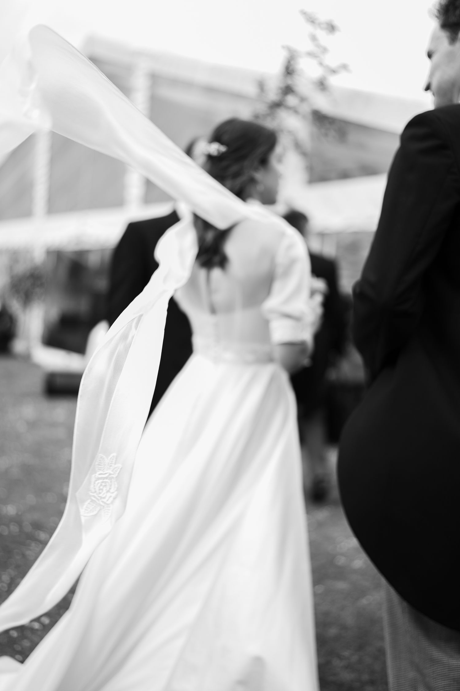 Black and white photo of a bride with flowing veil billowing in the wind at her wedding.